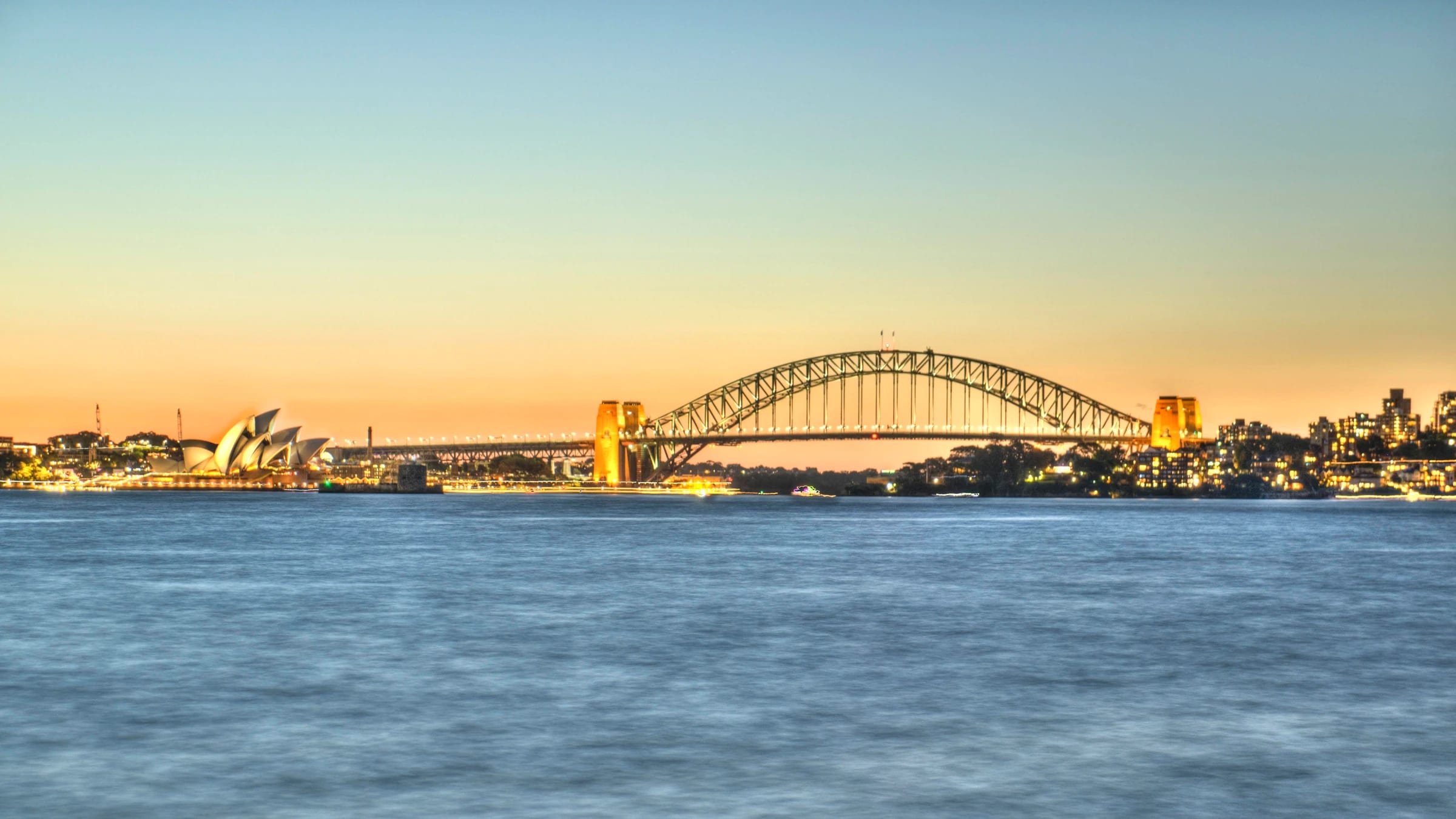 Sydney Opera House and Sydney Harbour Bridge across the harbour at dusk.
