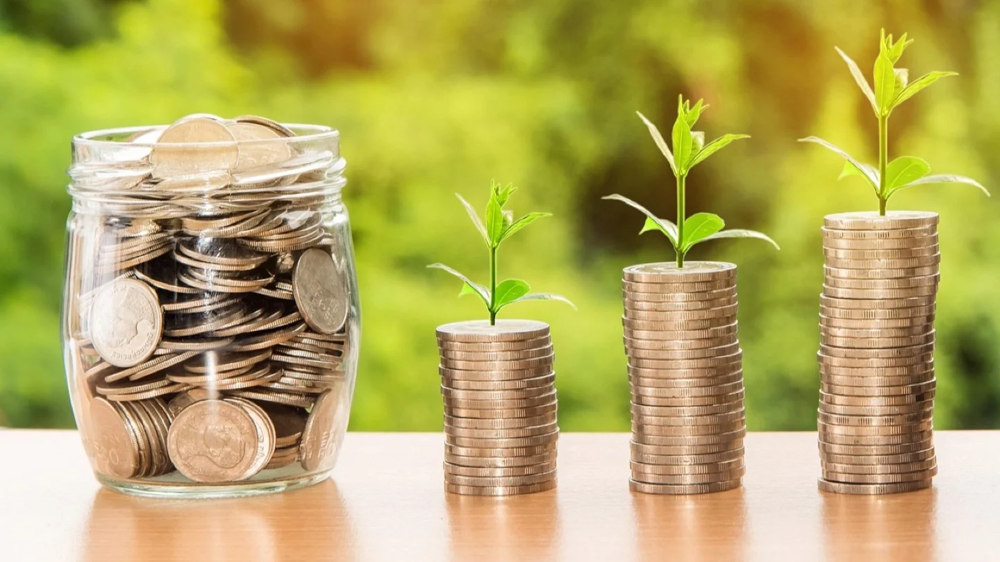 Young plants grow from progressively taller stacks of coins beside a jar of savings.