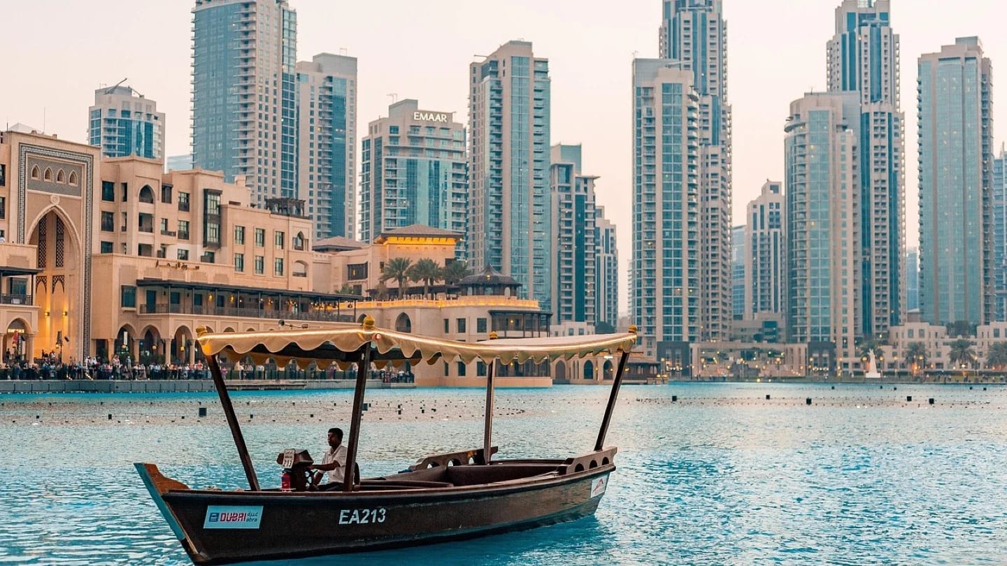 An abra crosses the water in downtown Dubai with high-rise buildings behind it.
