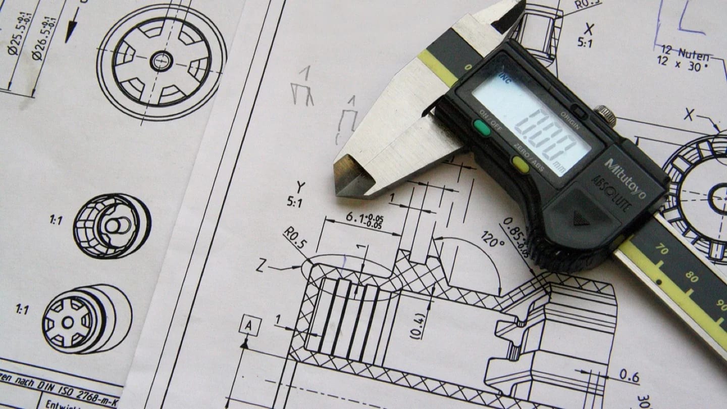 Digital calipers rest on a detailed mechanical engineering drawing.