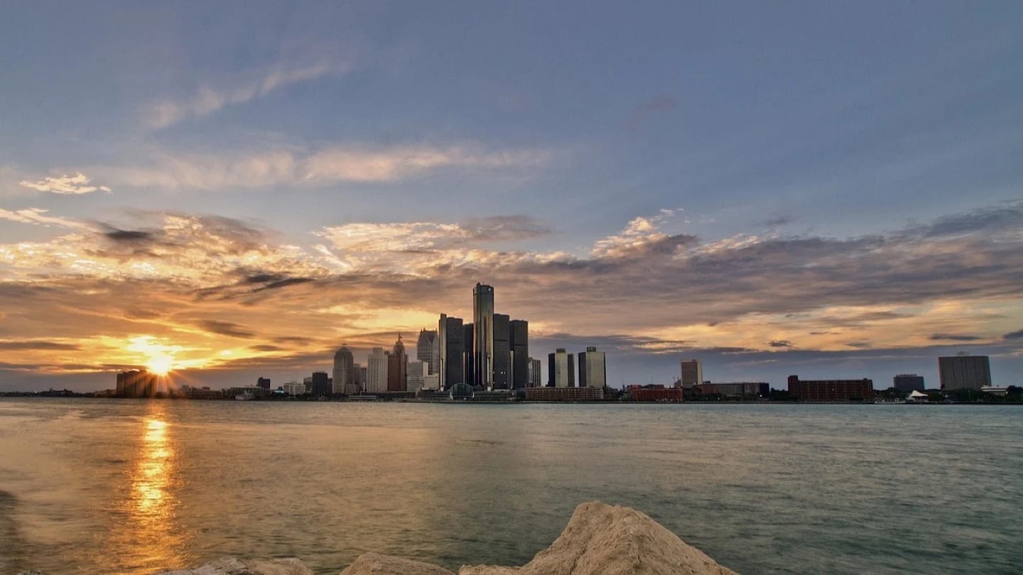 The Detroit skyline rises beyond the Detroit River at sunset.