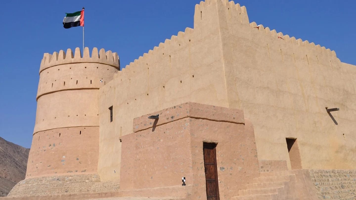 Fujairah Fort stands beneath a clear blue sky with the UAE flag above it.