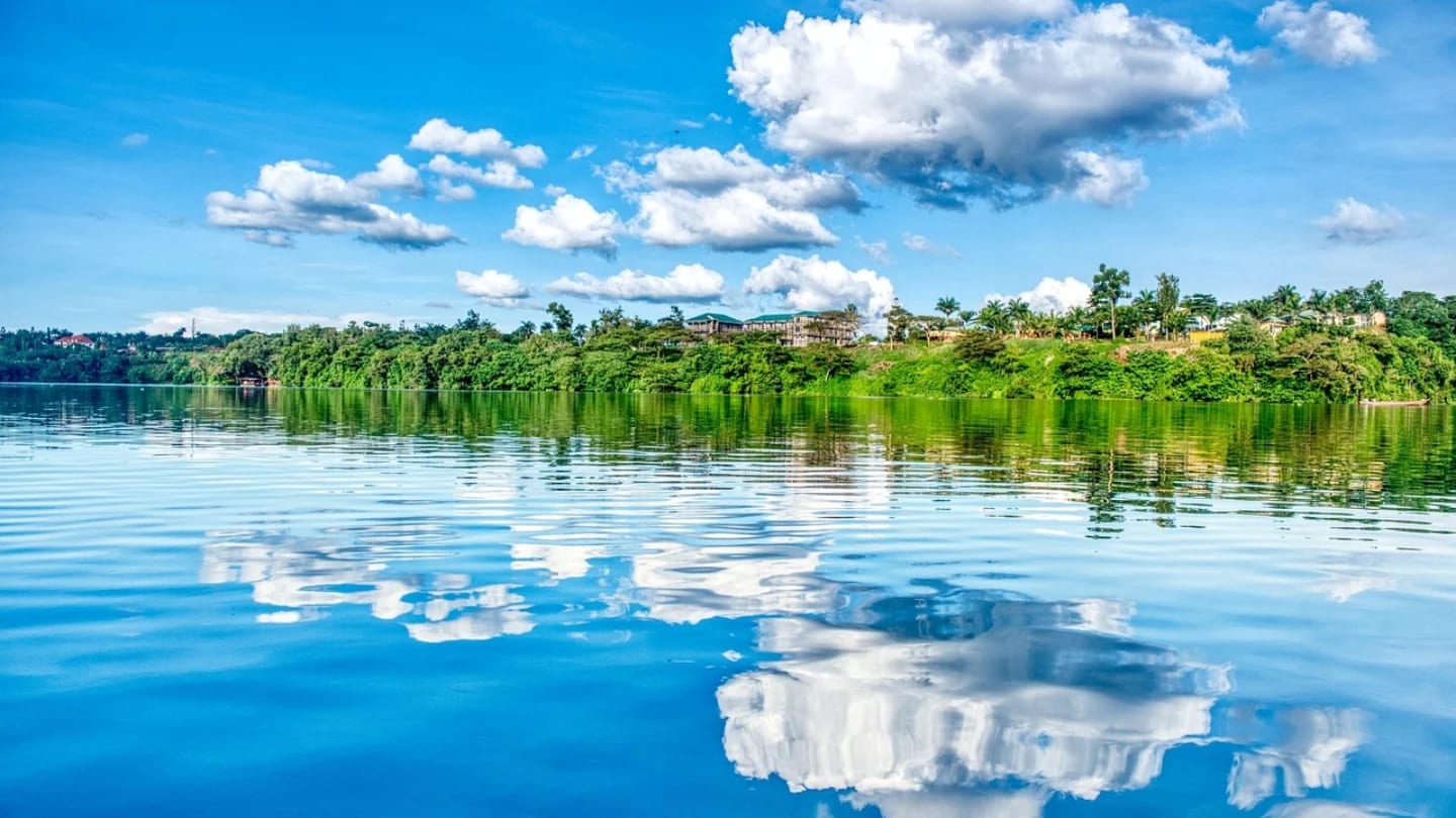 Wide view of the Nile River at Jinja, Uganda, with green banks and lakeside settlements under a blue sky.