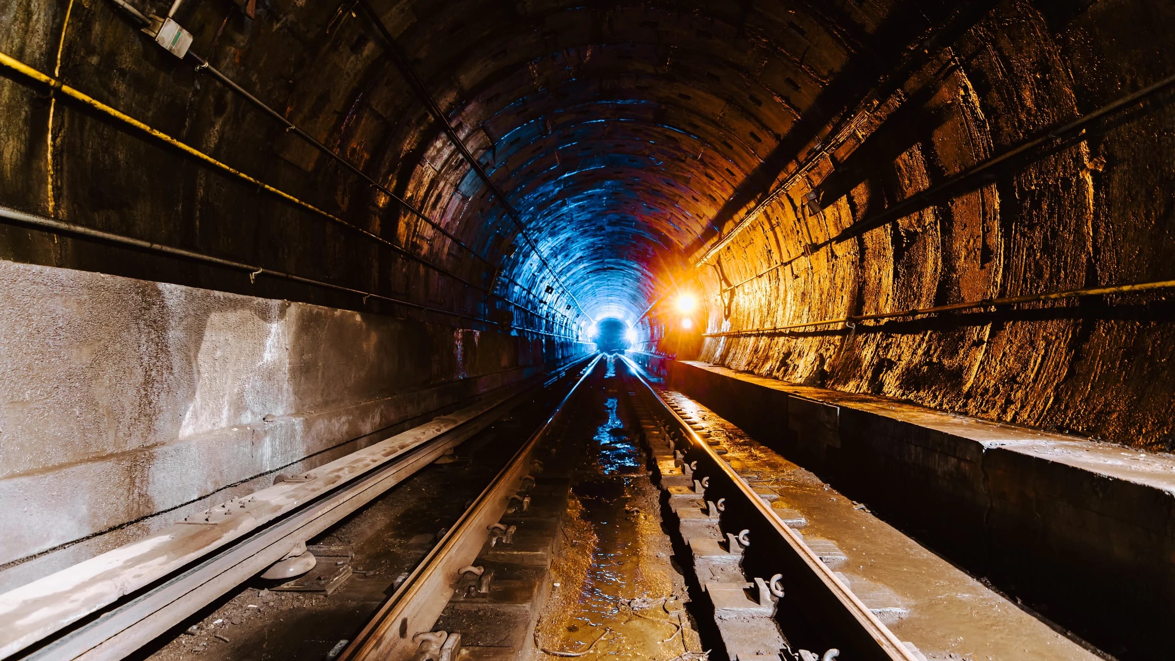 Rail tunnel receding toward a bright opening, with tracks and structural walls visible.