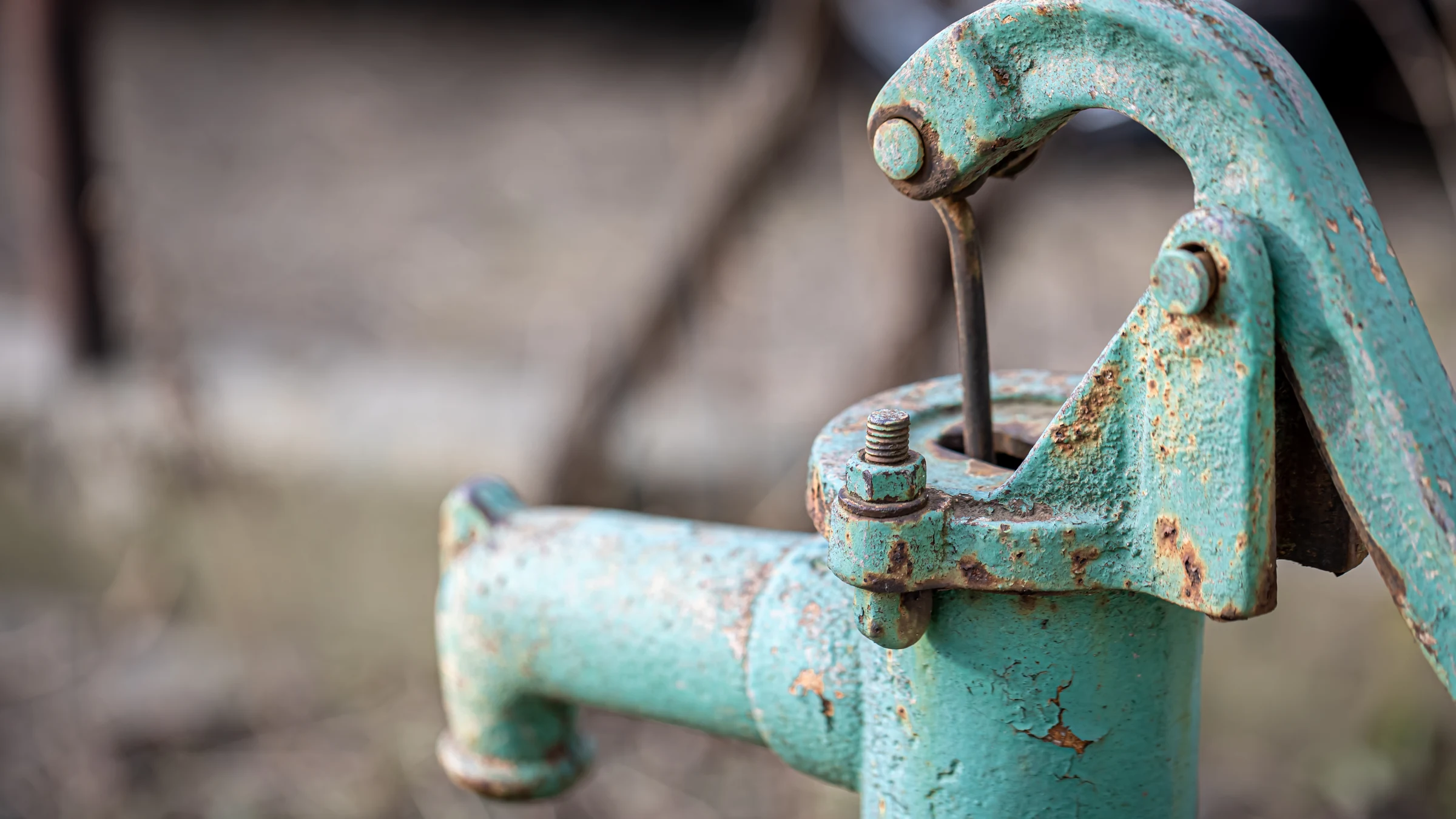 Close view of a weathered blue-green outdoor water pump with rusted fittings.