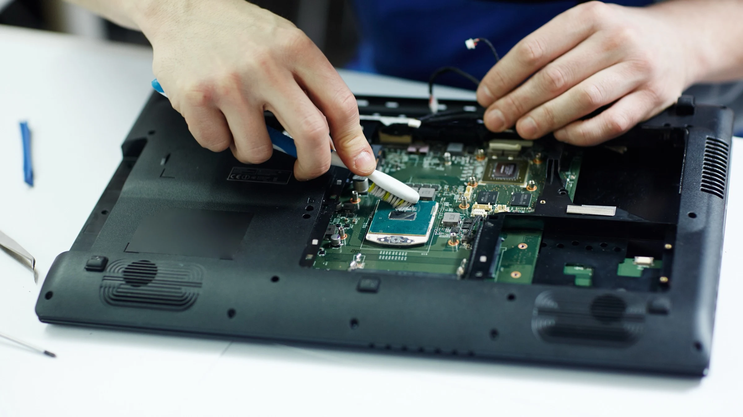 Technician cleaning the circuit board of a disassembled laptop