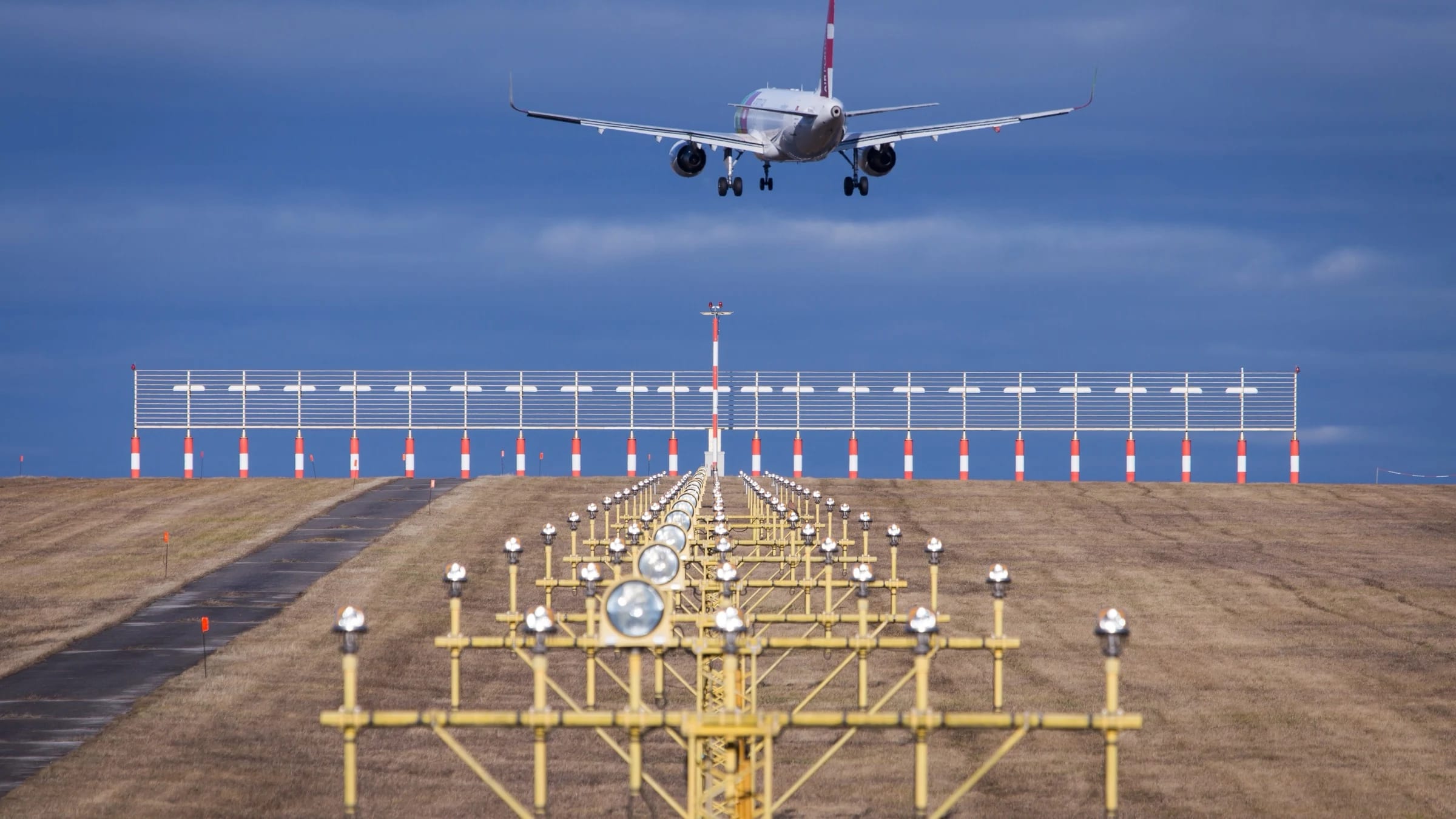 Aircraft approaches a runway lined with illuminated navigation lights at dusk.