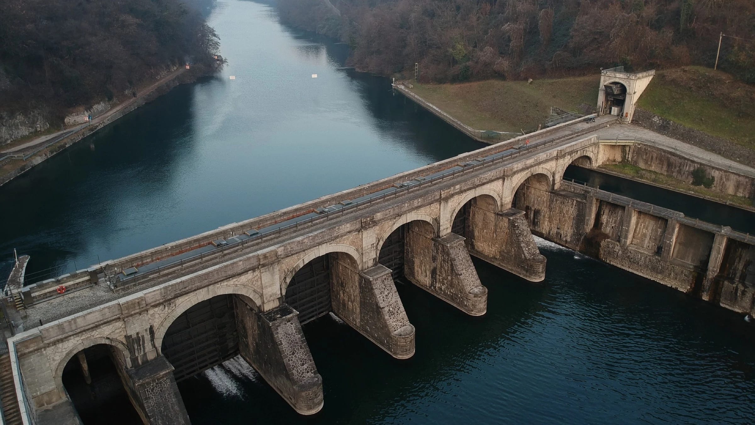 Aerial view of a gated dam and reservoir in a wooded valley.