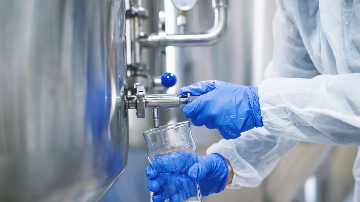 Operator in protective gloves taking a liquid sample from industrial treatment equipment