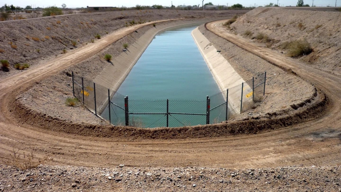 Concrete-lined water conveyance canal curving through dry, arid terrain.