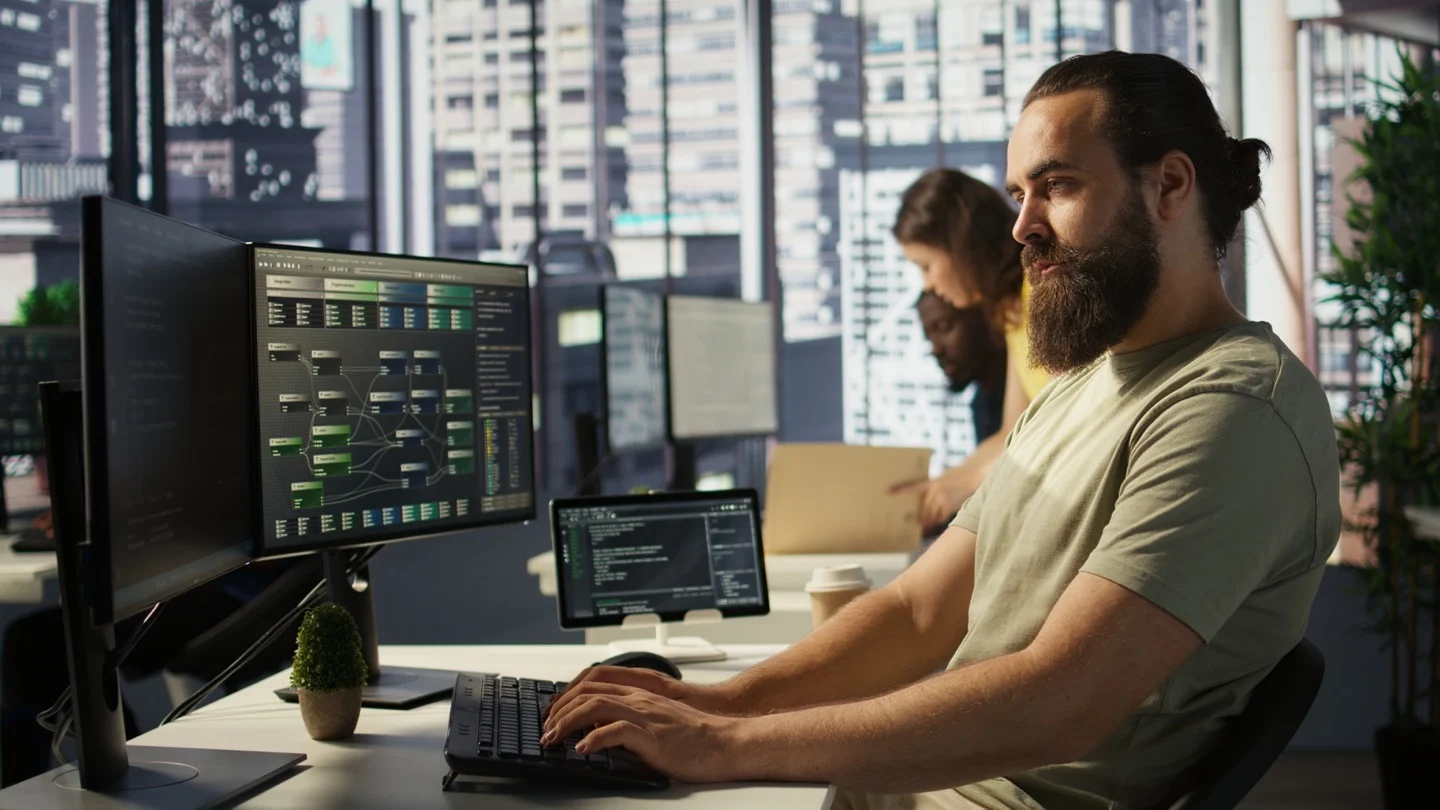 A machine-learning infrastructure engineer works beside computer screens displaying code and technical data.