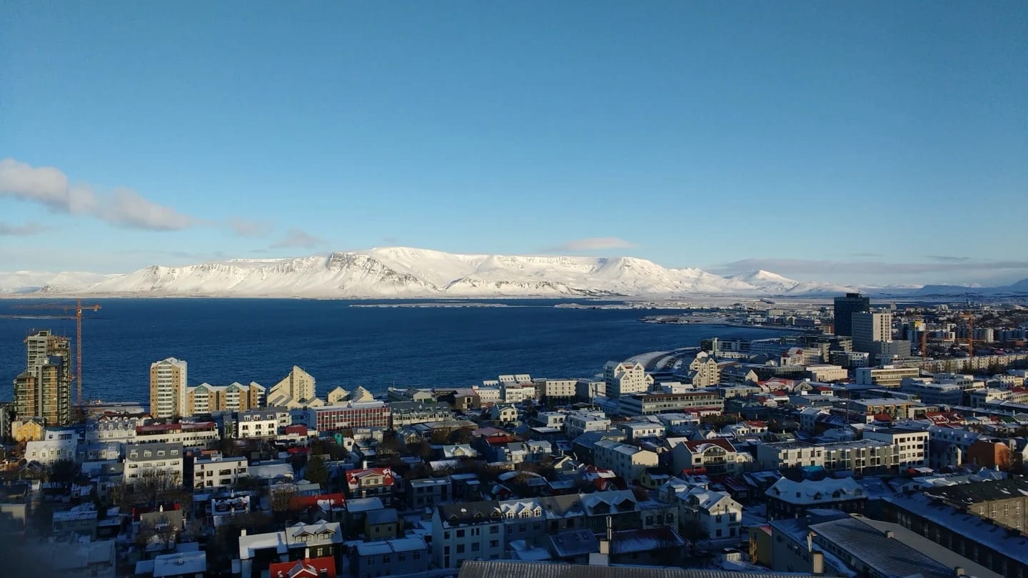 Reykjavík extends along Iceland’s coast beneath snow-covered mountains and a clear blue sky.