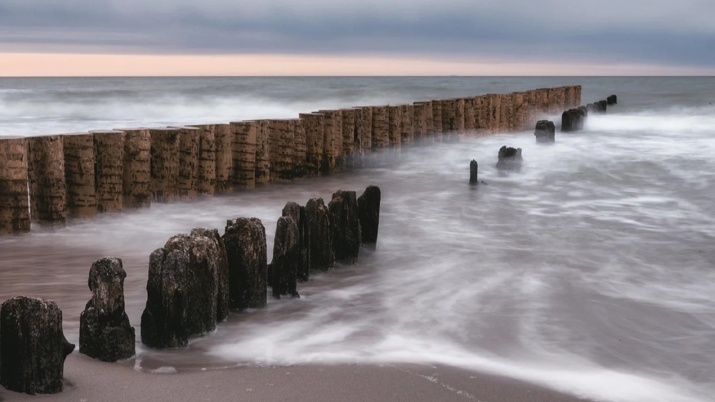 Rows of timber coastal barriers extend into rough seawater.