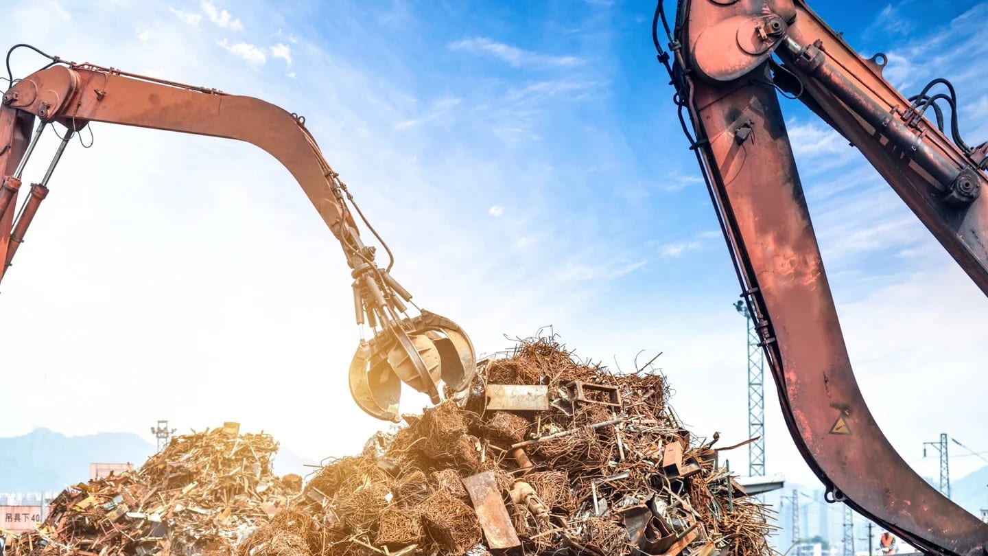 Industrial cranes work above large piles of mixed scrap metal at a recycling yard.
