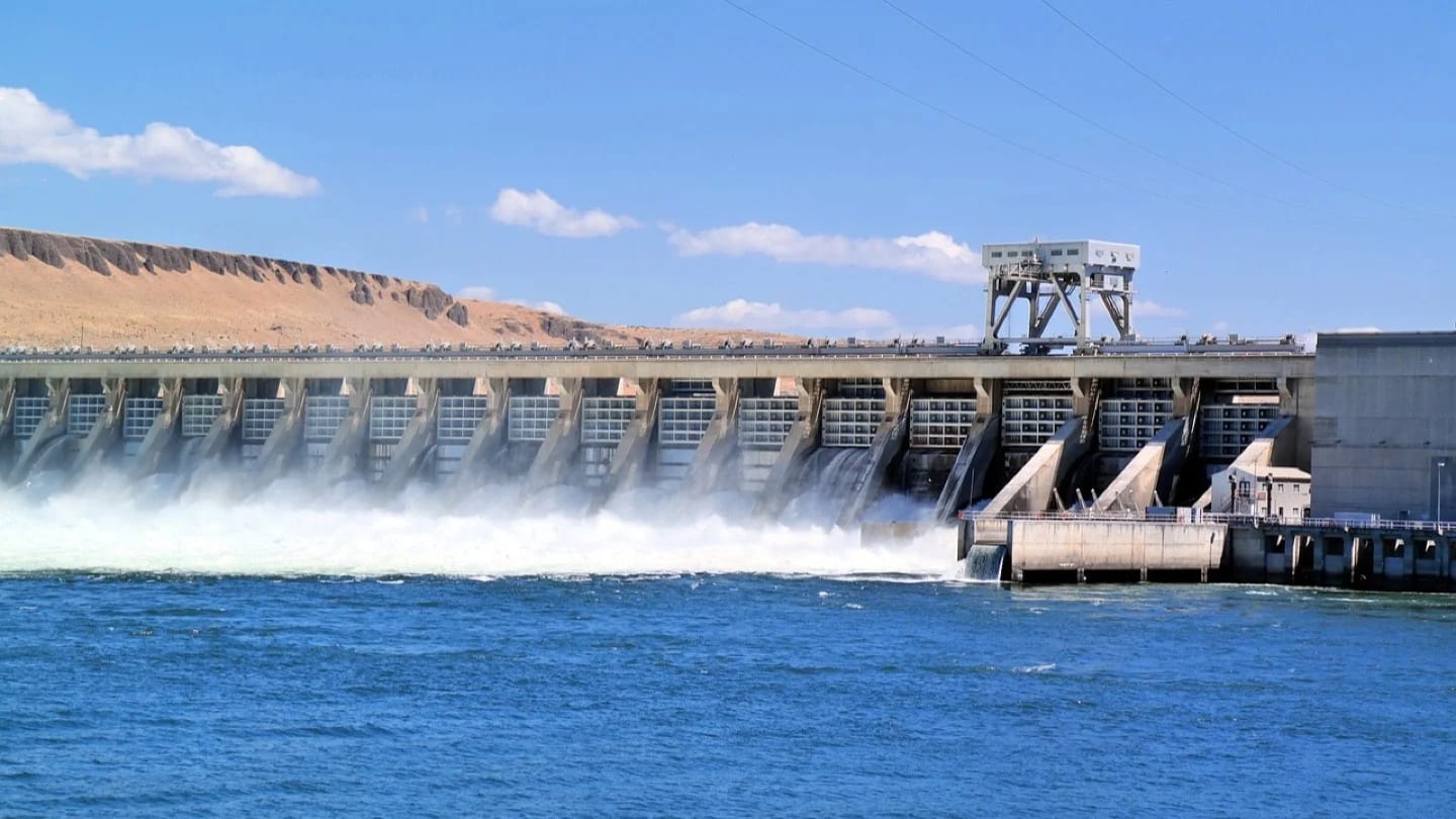 Large concrete dam releases water into a broad river.