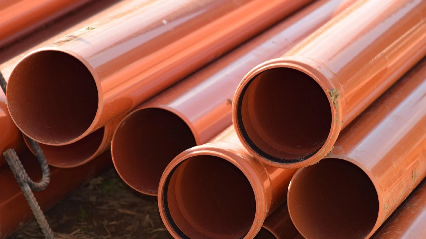 Stacks of orange sewer pipes await installation at a construction site.