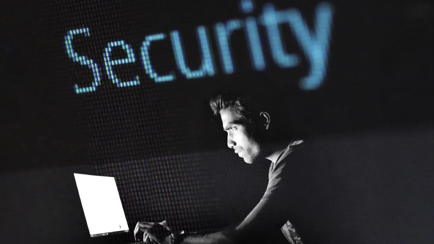 A cybersecurity professional works at a laptop against a dark digital security display.