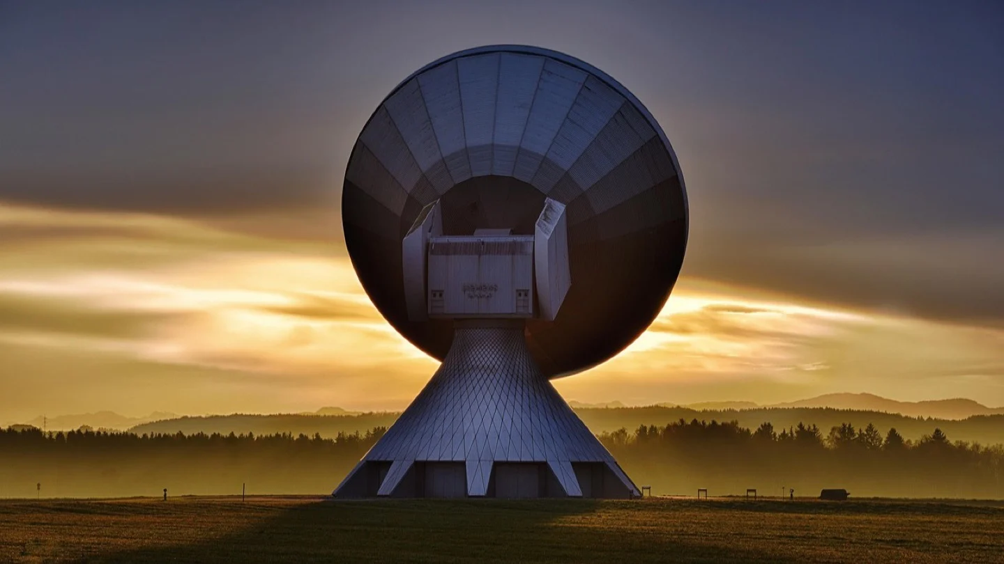 A large radio telescope stands against a glowing sunset sky.