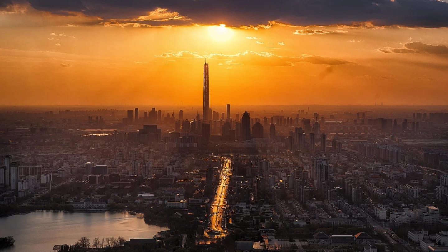 Aerial view of a dense city skyline under an intense orange sun at dusk.