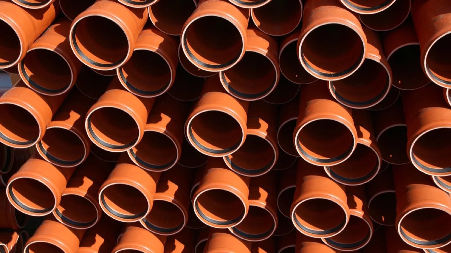 Rows of large orange infrastructure pipes stacked for installation.