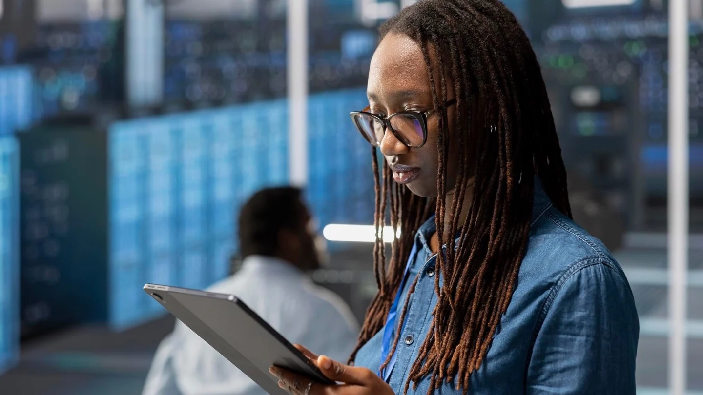 A data-center engineer uses a tablet beside server racks.