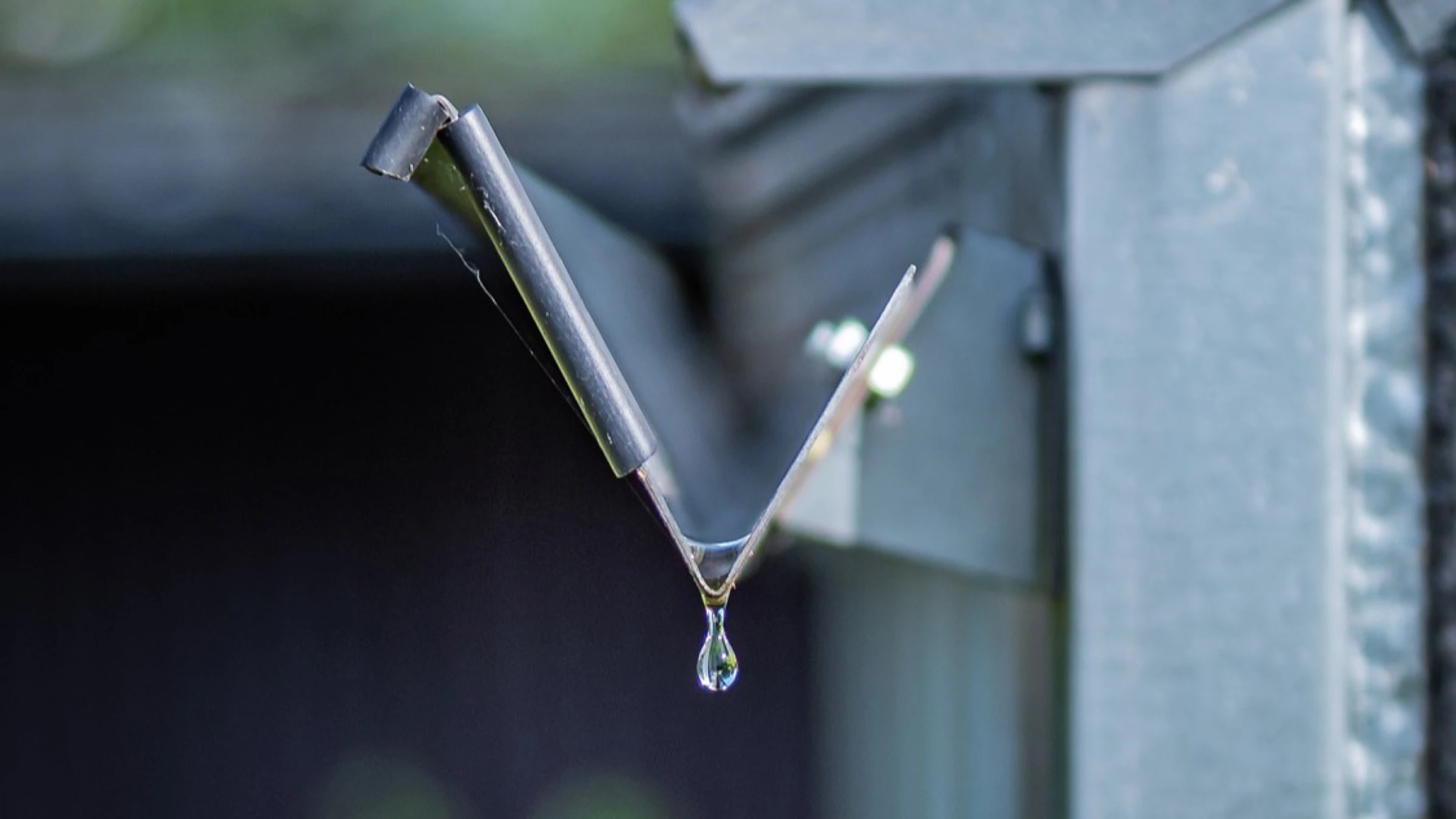 A drop of rainwater falling from a metal gutter outlet.