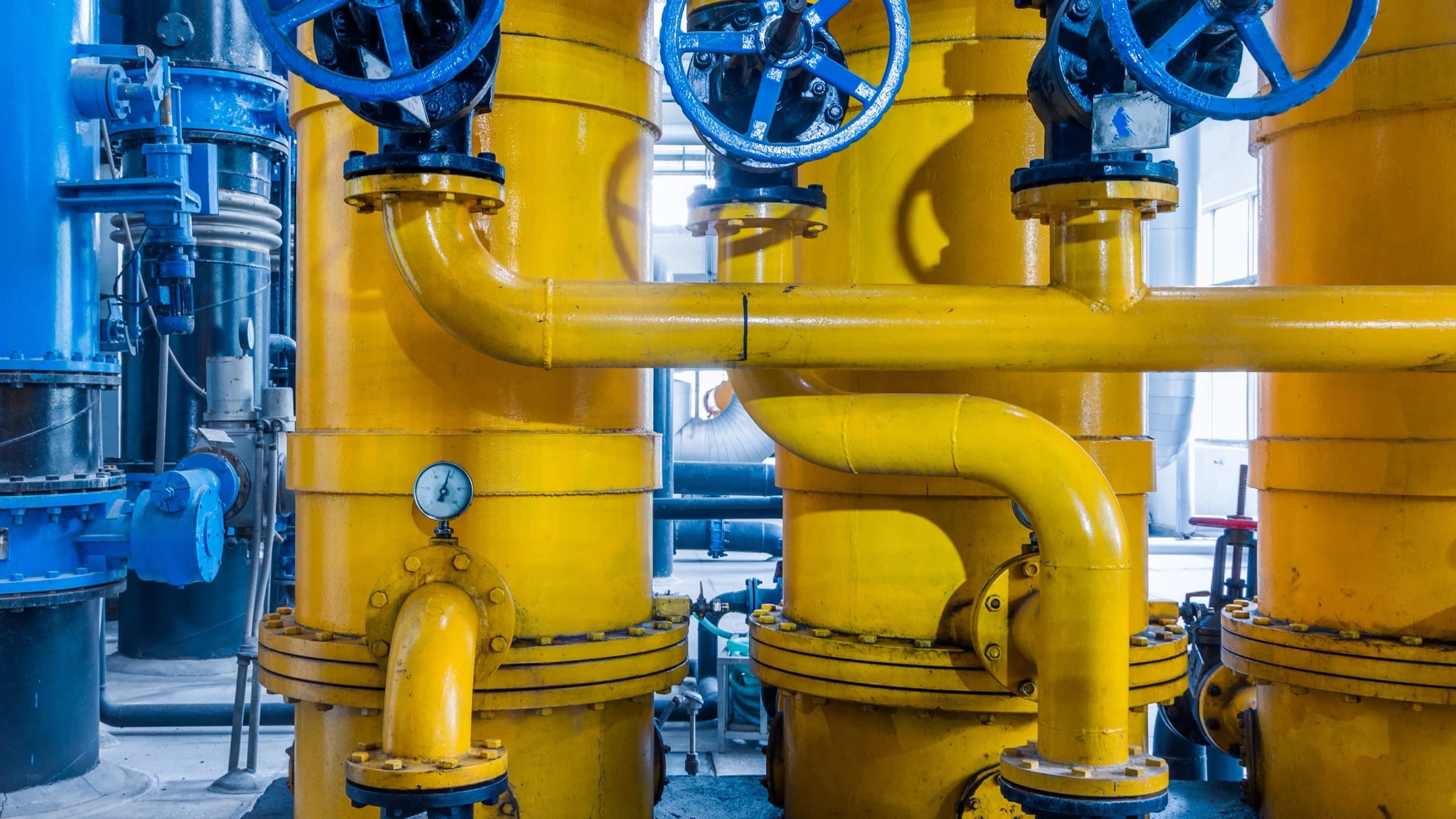 Large yellow industrial gas pipes and blue valves inside a processing plant.