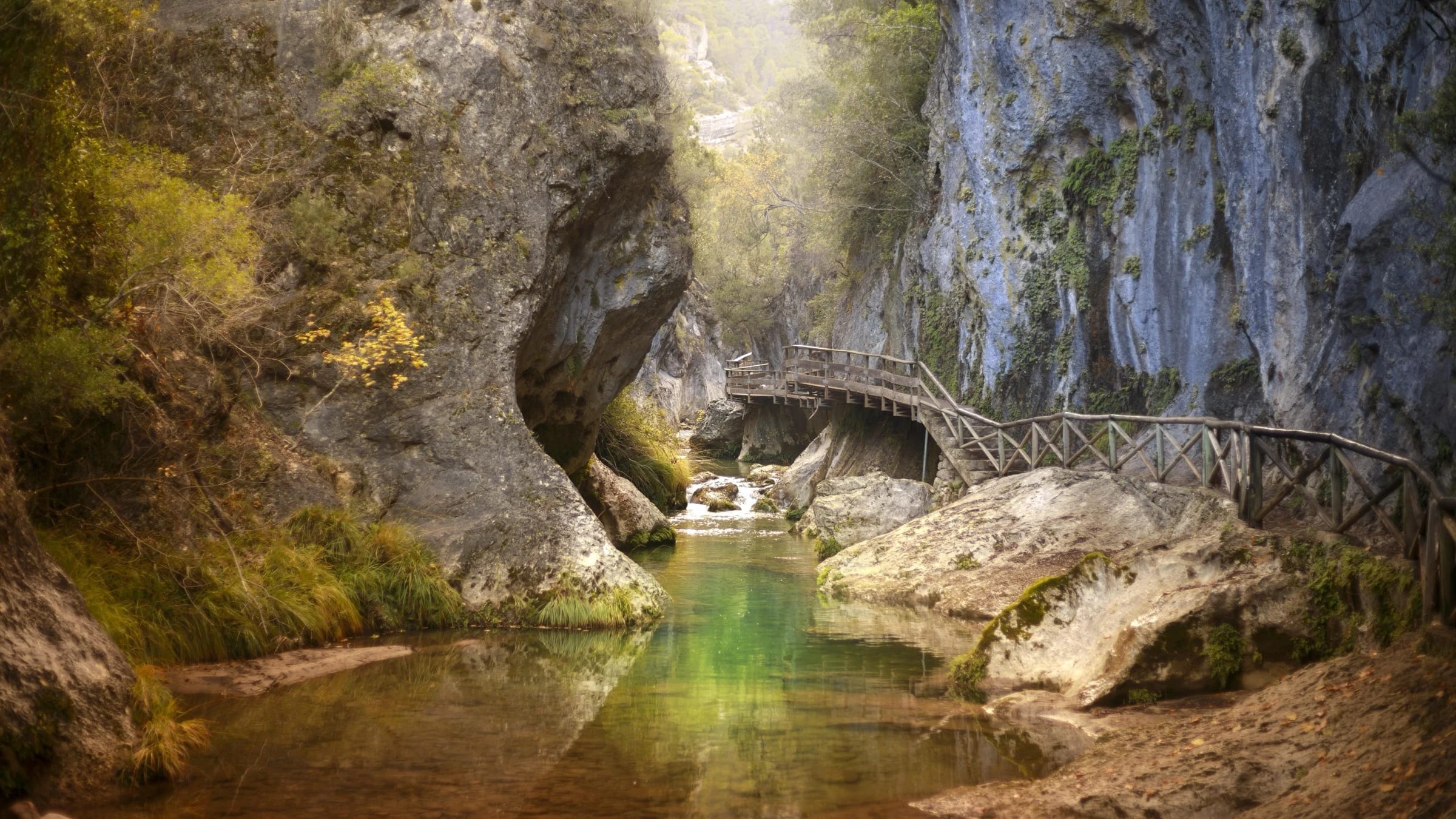 Rocky river channel and wooden walkway in a forested gorge in Jaén, Spain.