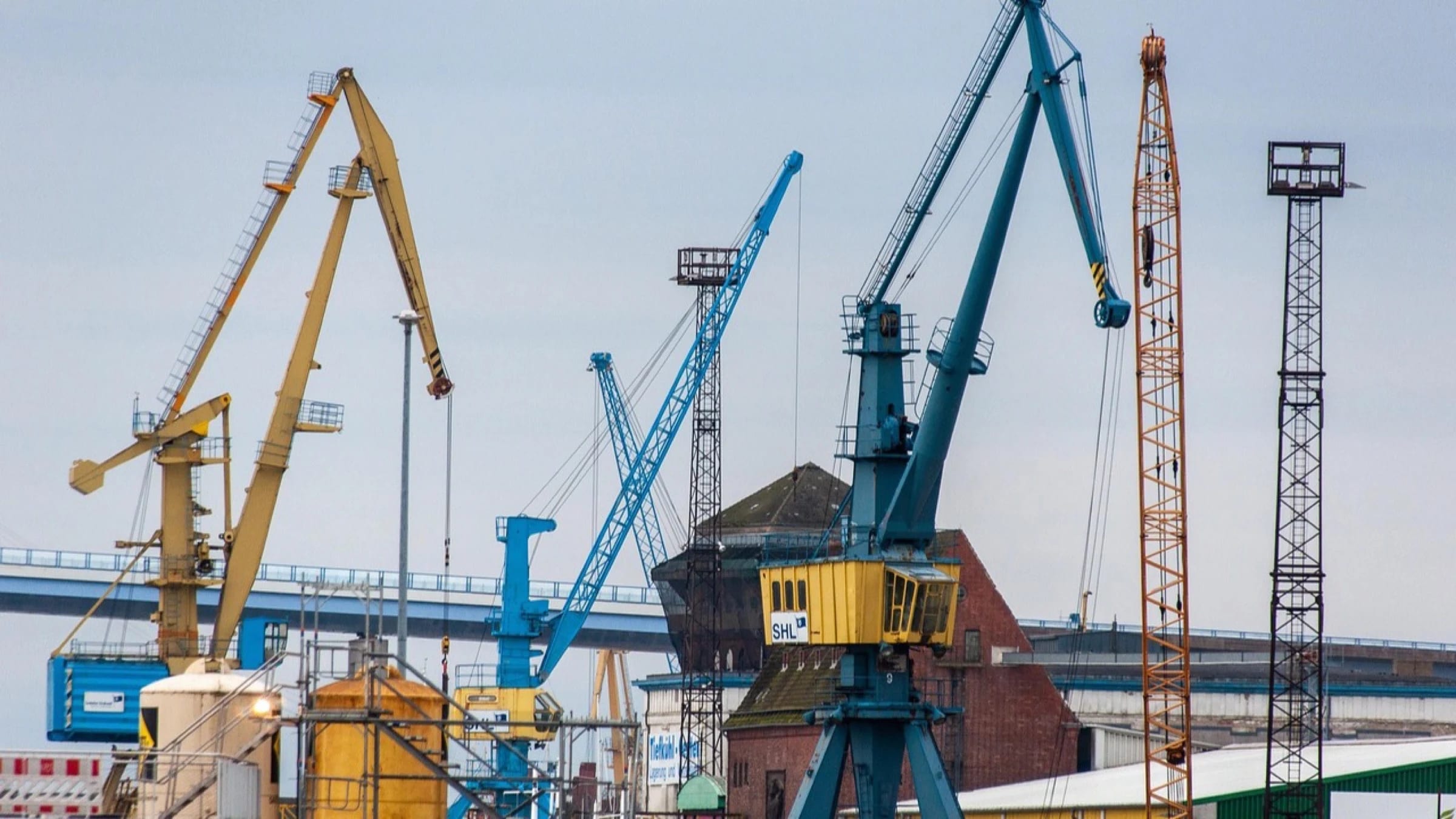 Multiple construction cranes operating beside an industrial port.