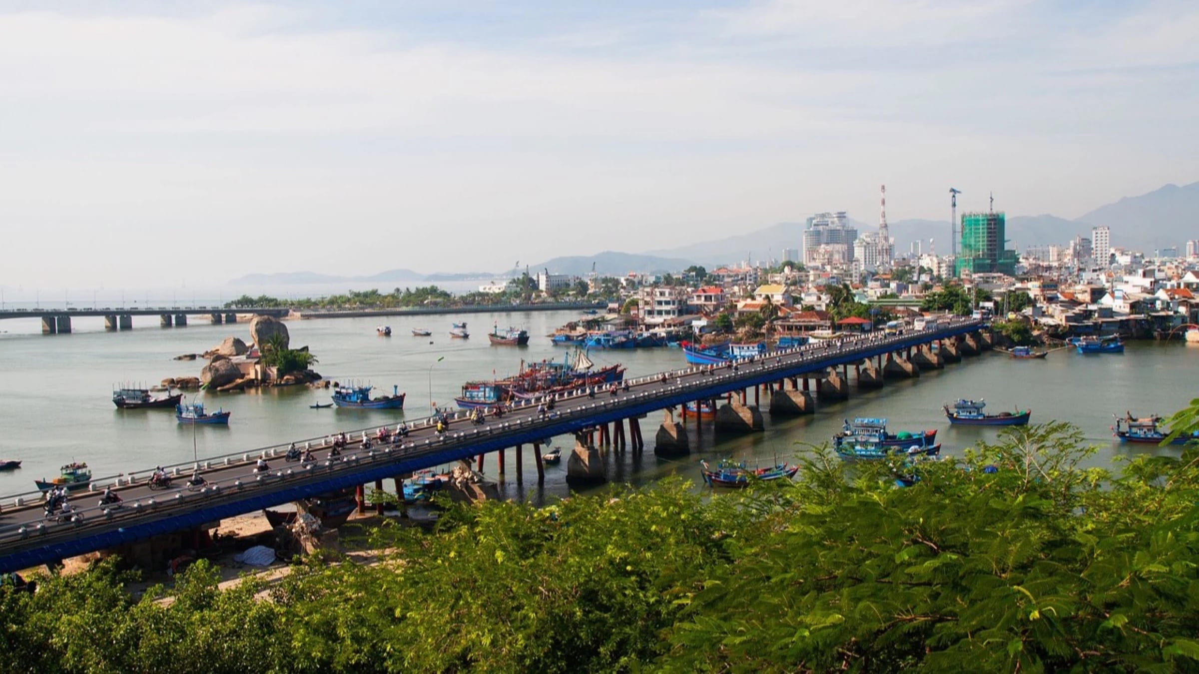 Boats on a river beside a bridge and port infrastructure in Viet Nam.