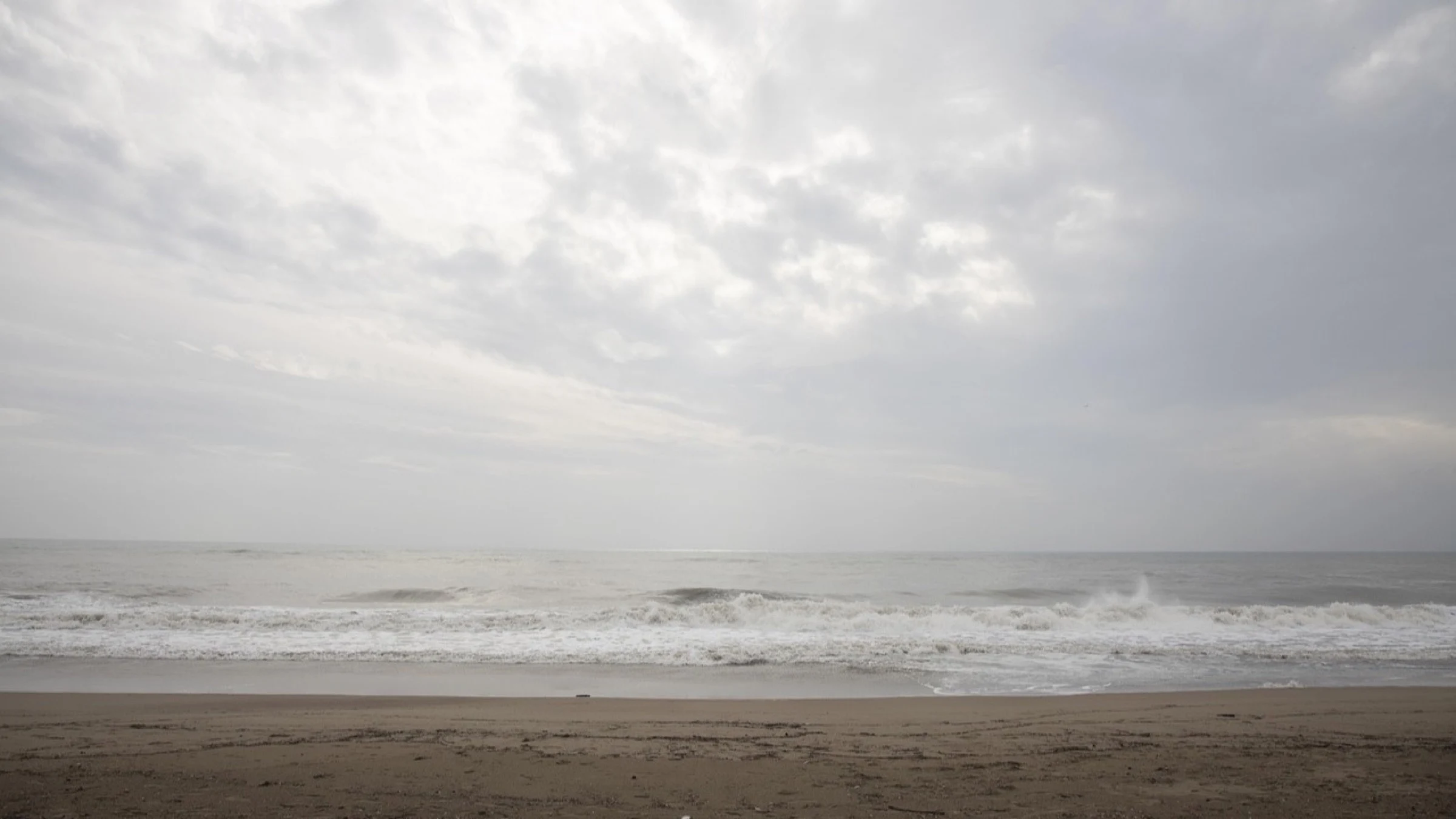 Waves breaking along an exposed coast beneath an overcast sky.