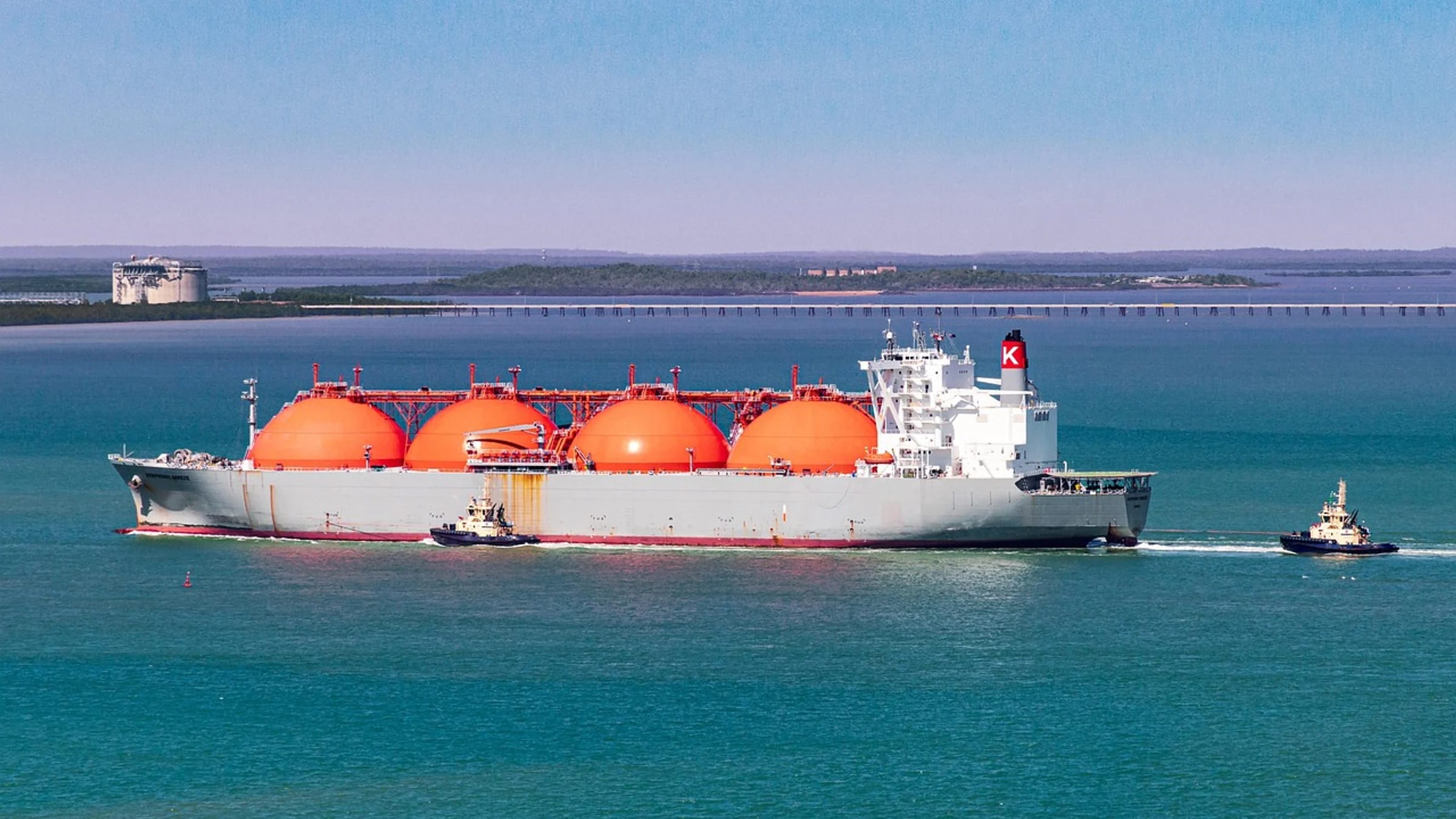 An LNG carrier with spherical gas tanks escorted by tugboats.