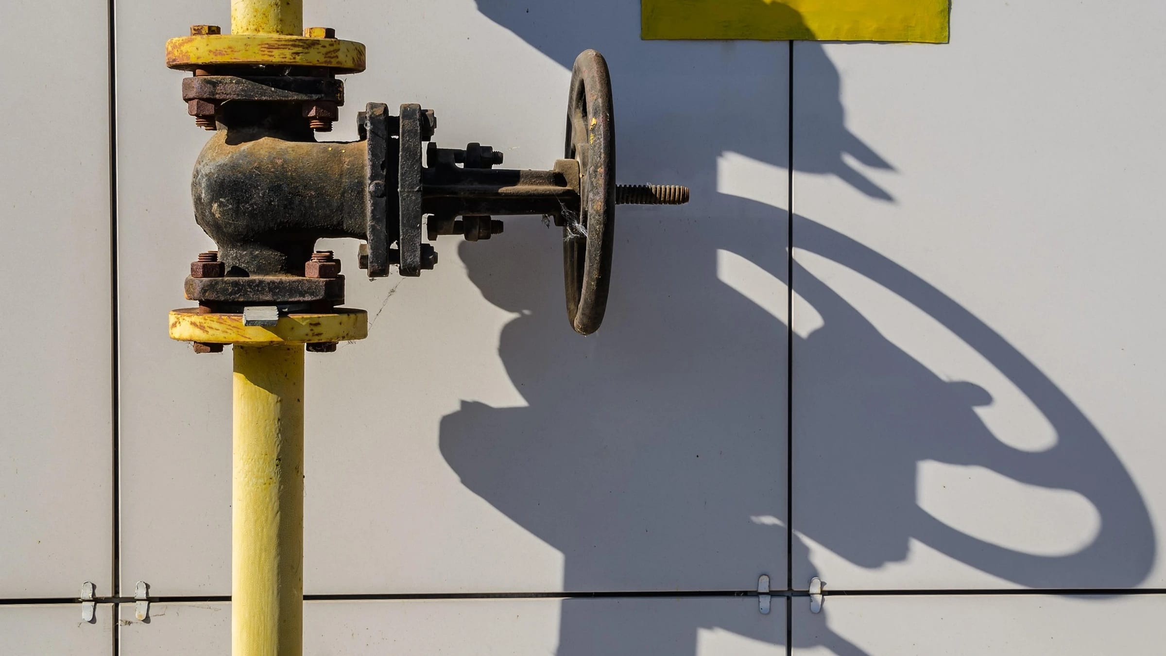 Yellow gas pipe with a metal valve and handwheel against a wall.