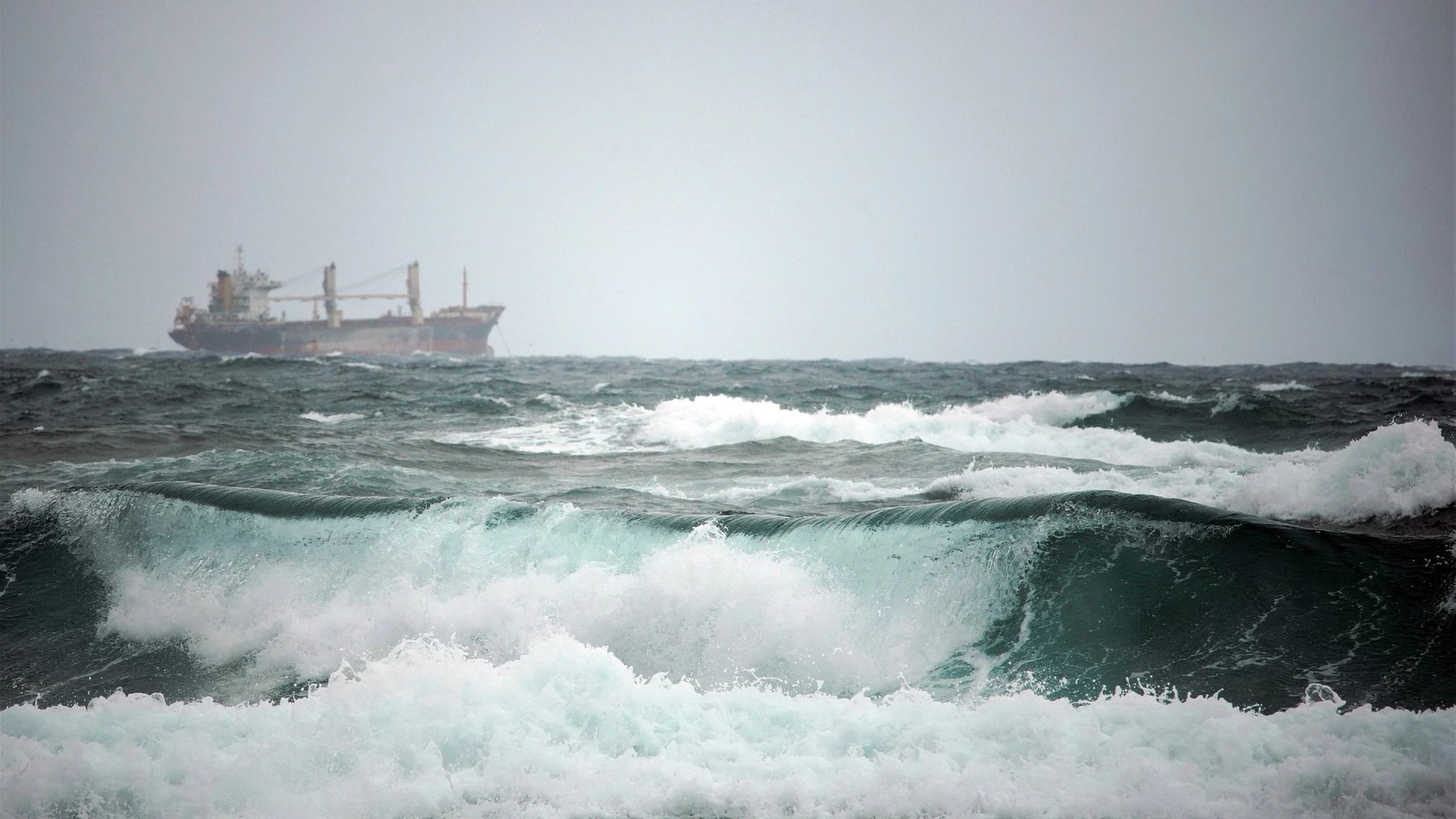 Cargo vessel beyond waves in rough sea