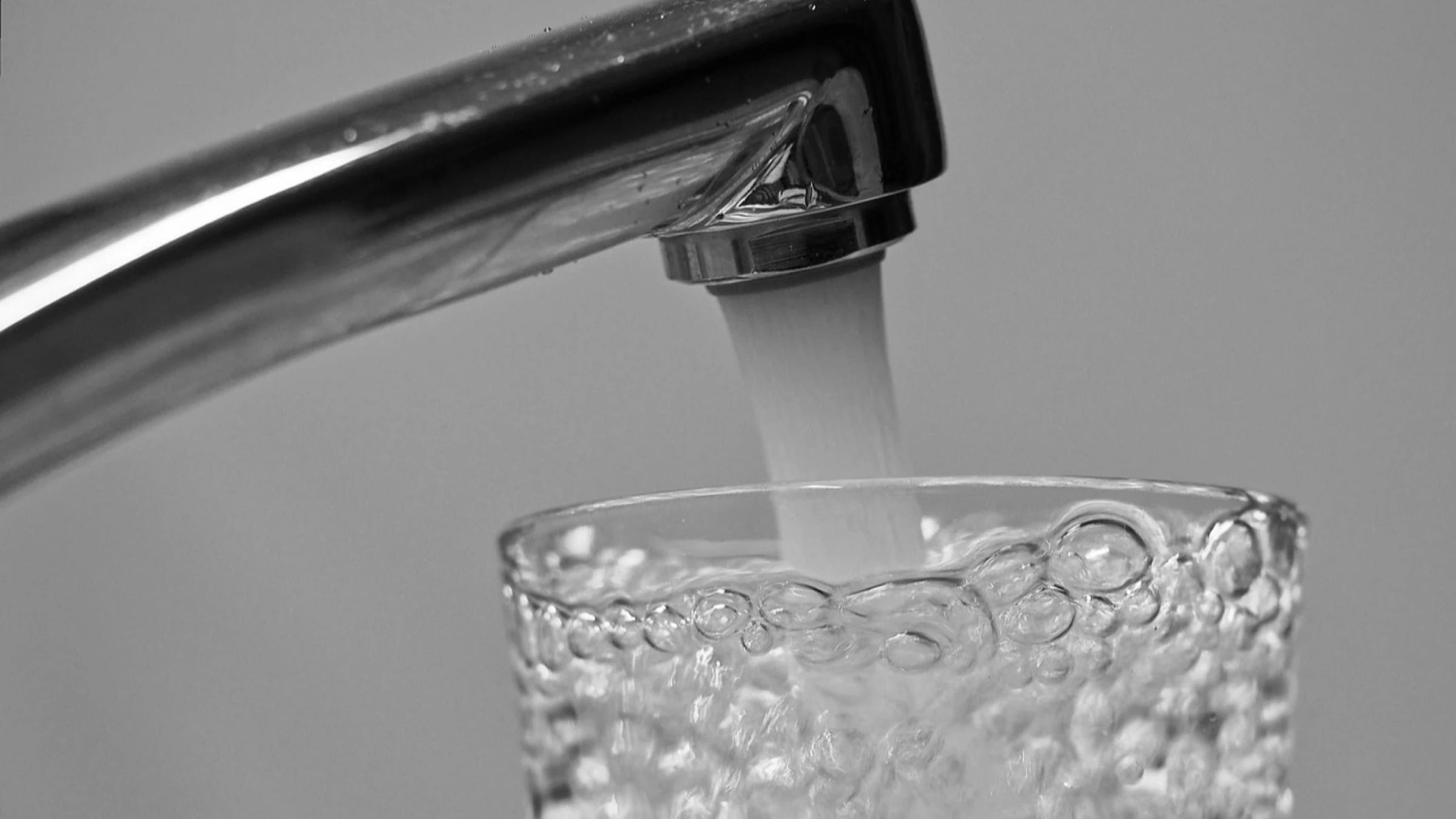 Water flowing from a tap into a drinking glass.