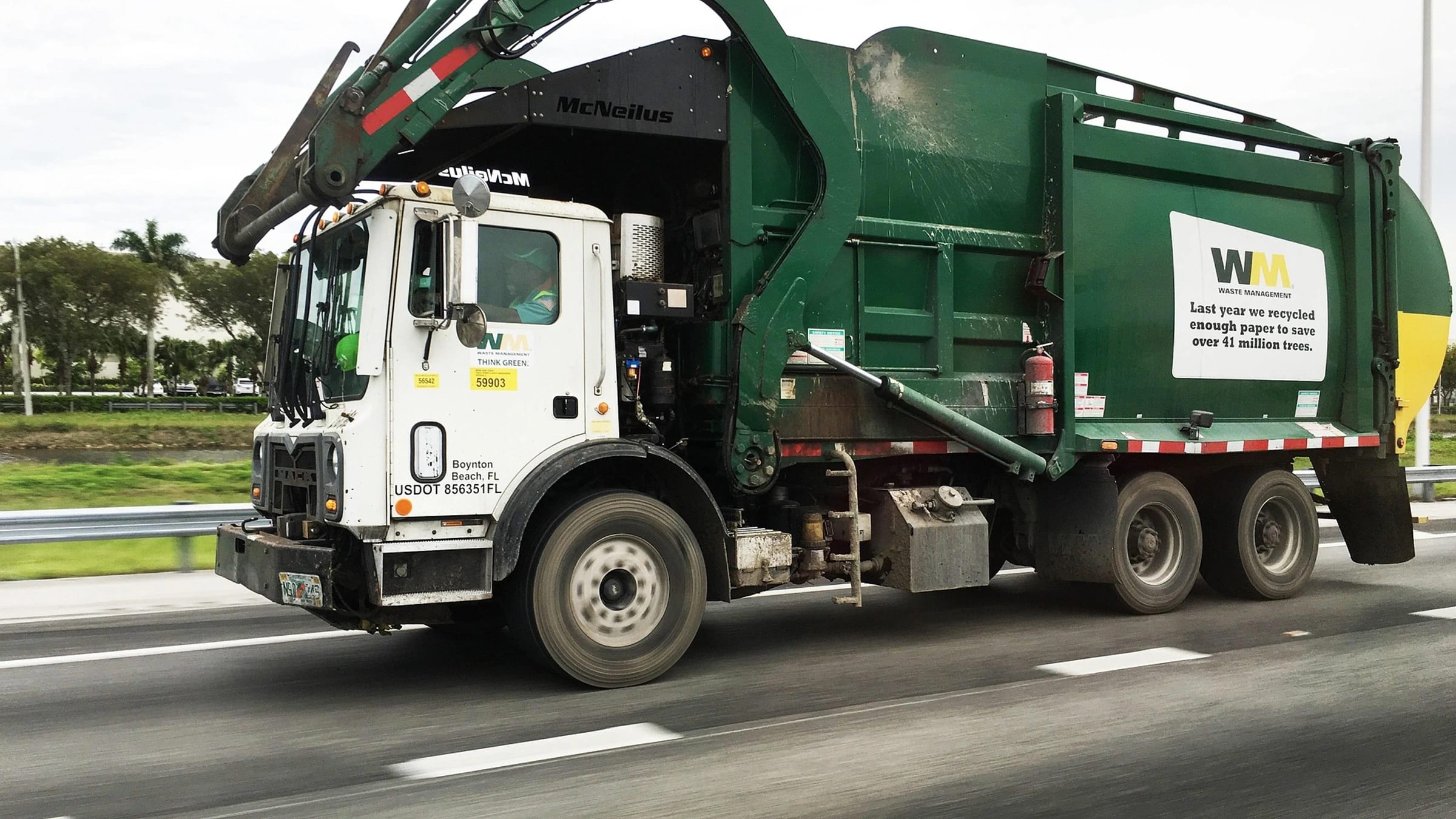 A green waste-collection truck traveling on a highway.