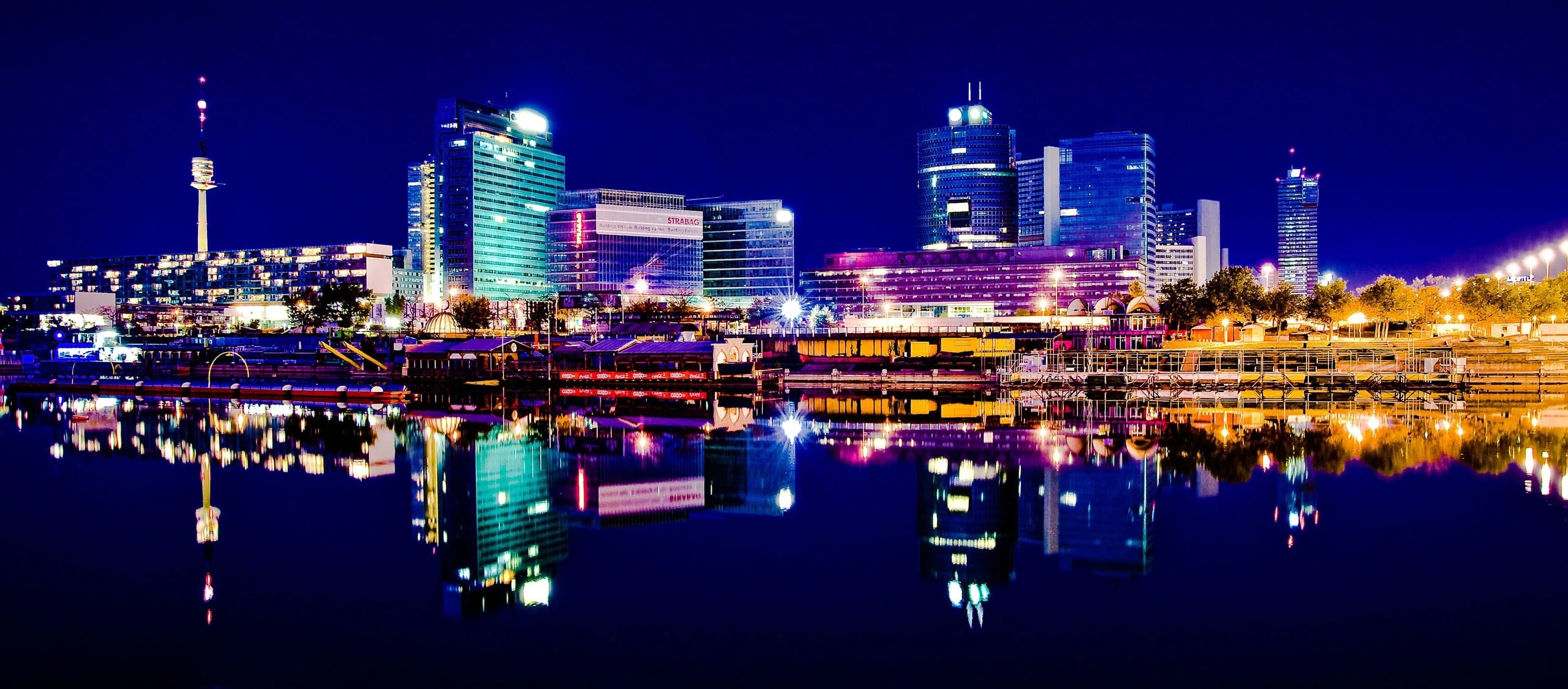 Illuminated buildings and the Danube Tower reflected in the water in Vienna at night.