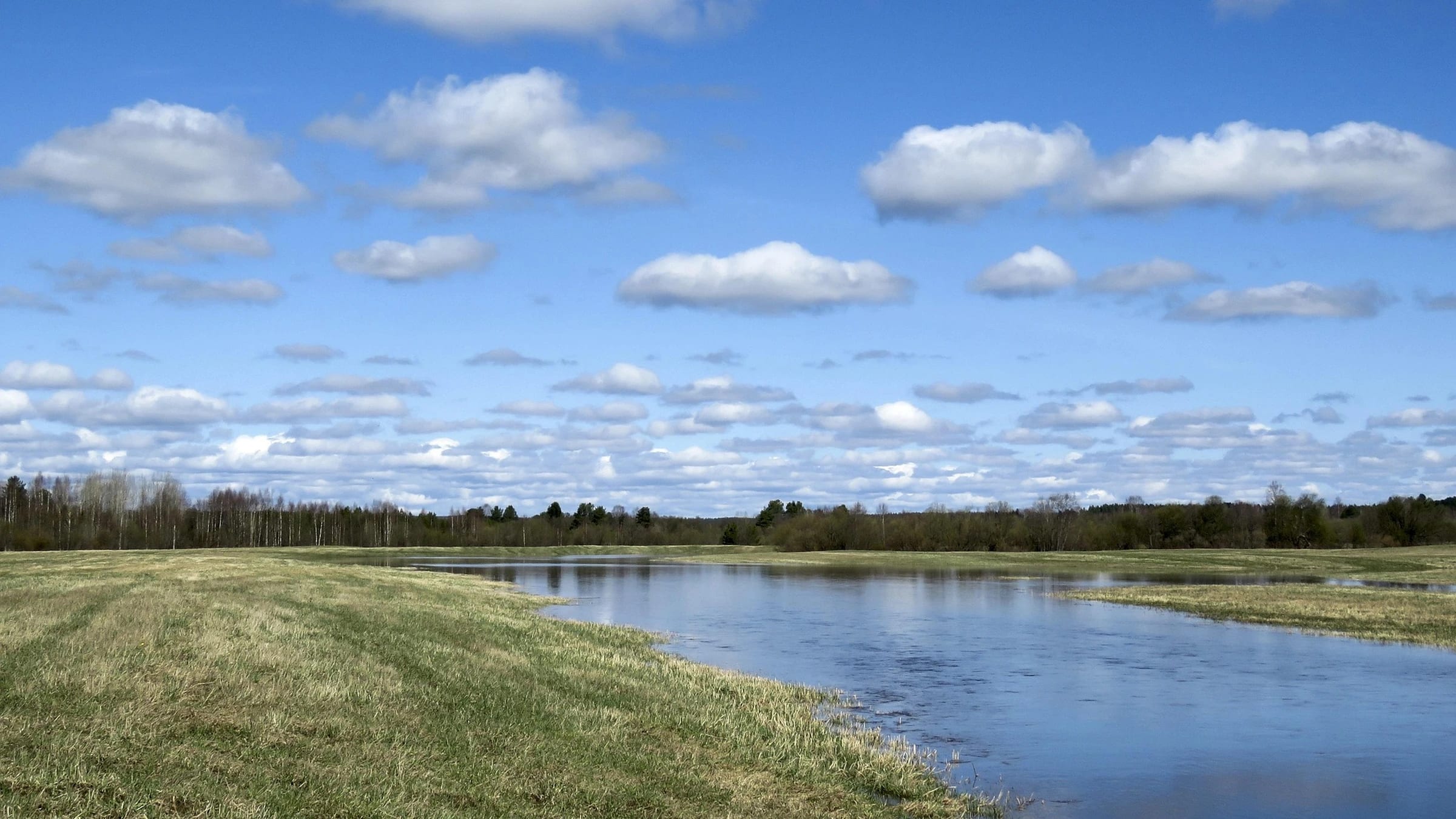 River beside a grassy floodplain under a cloudy sky