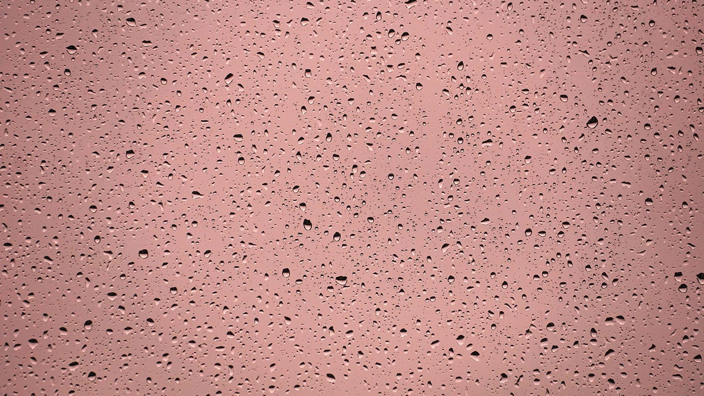 Raindrops across a window against a muted pink background.