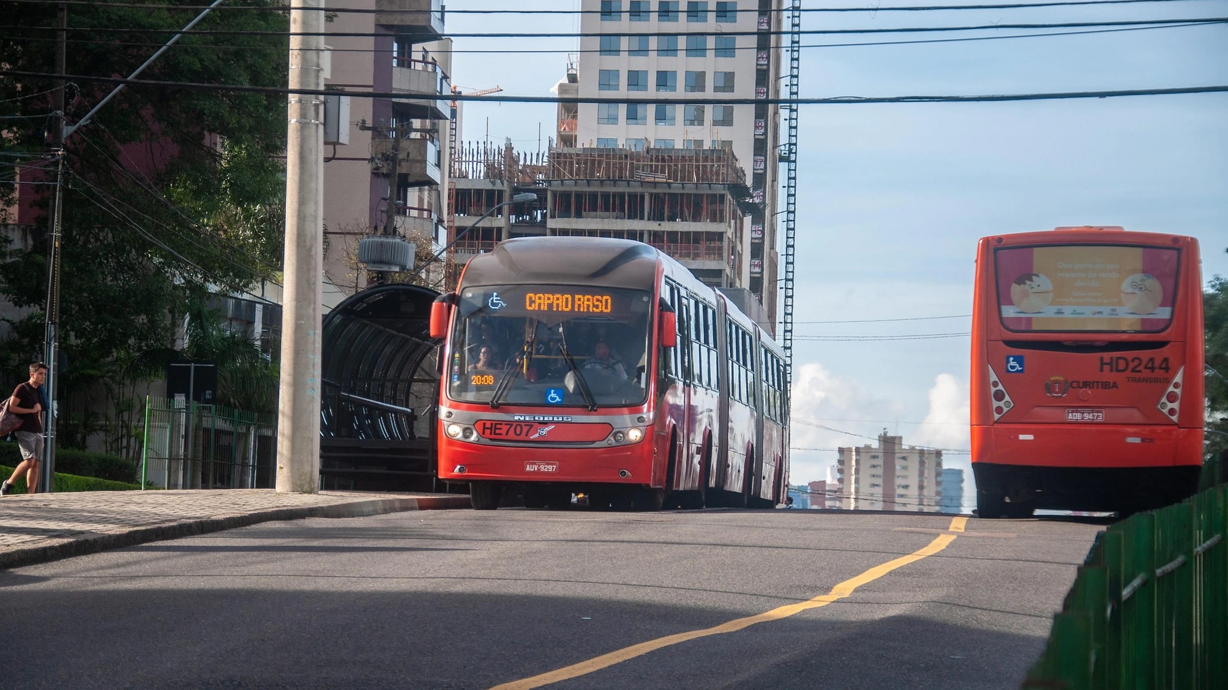 Red buses on a Curitiba street beside a tube bus station