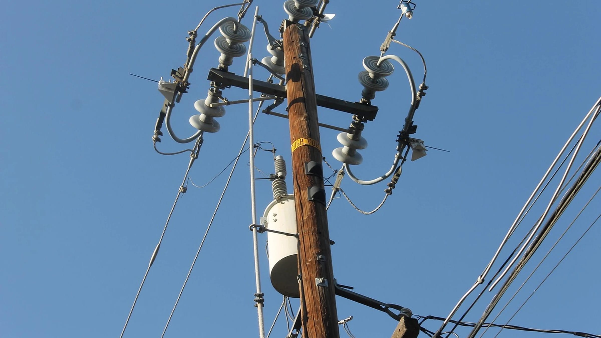 Pole-mounted transformer and overhead electricity wires against blue sky