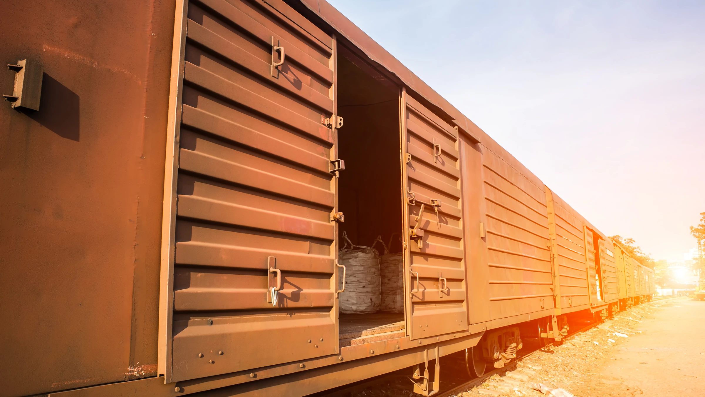 Freight locomotive hauling stacked containers along a rail corridor.