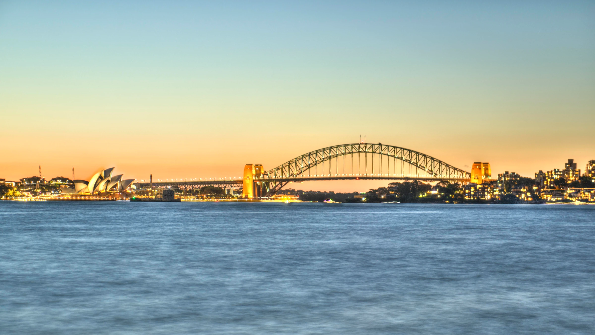 Sydney Opera House and Sydney Harbour Bridge across the harbour at dusk.