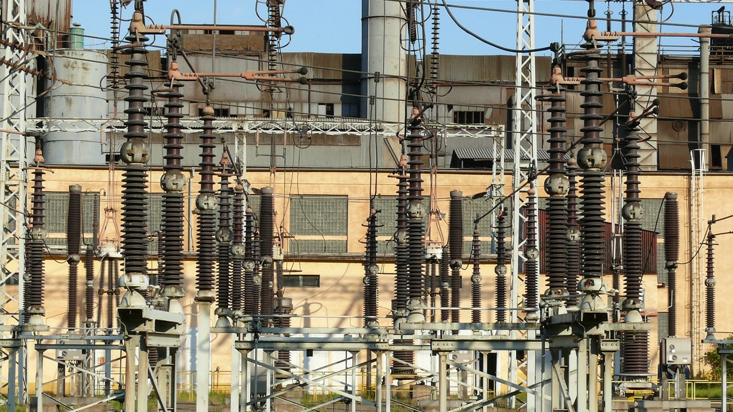 High-voltage electrical substation with switchgear, insulators and overhead conductors.