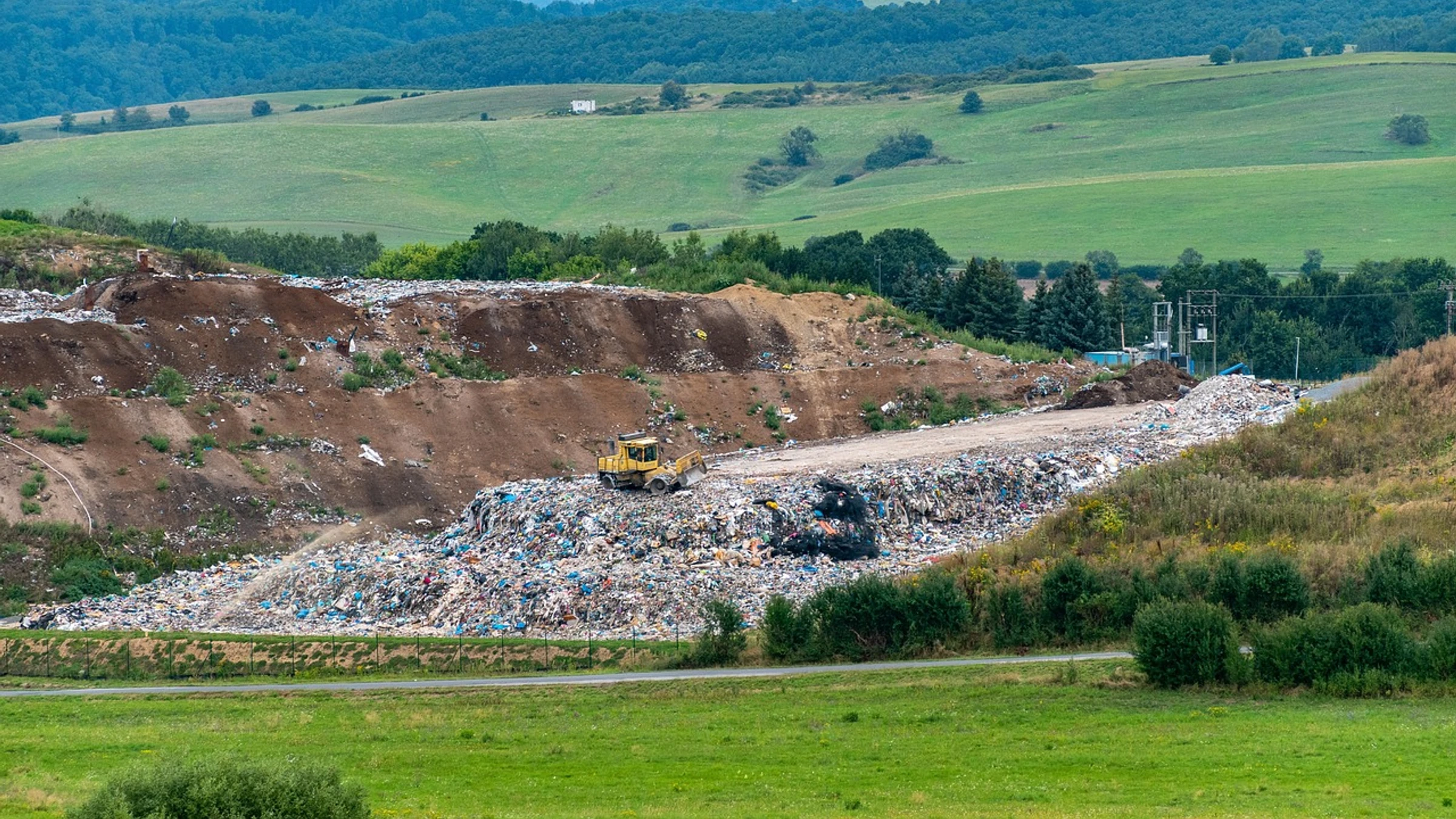 A landfill with earthmoving machinery and waste piles in a rural landscape.