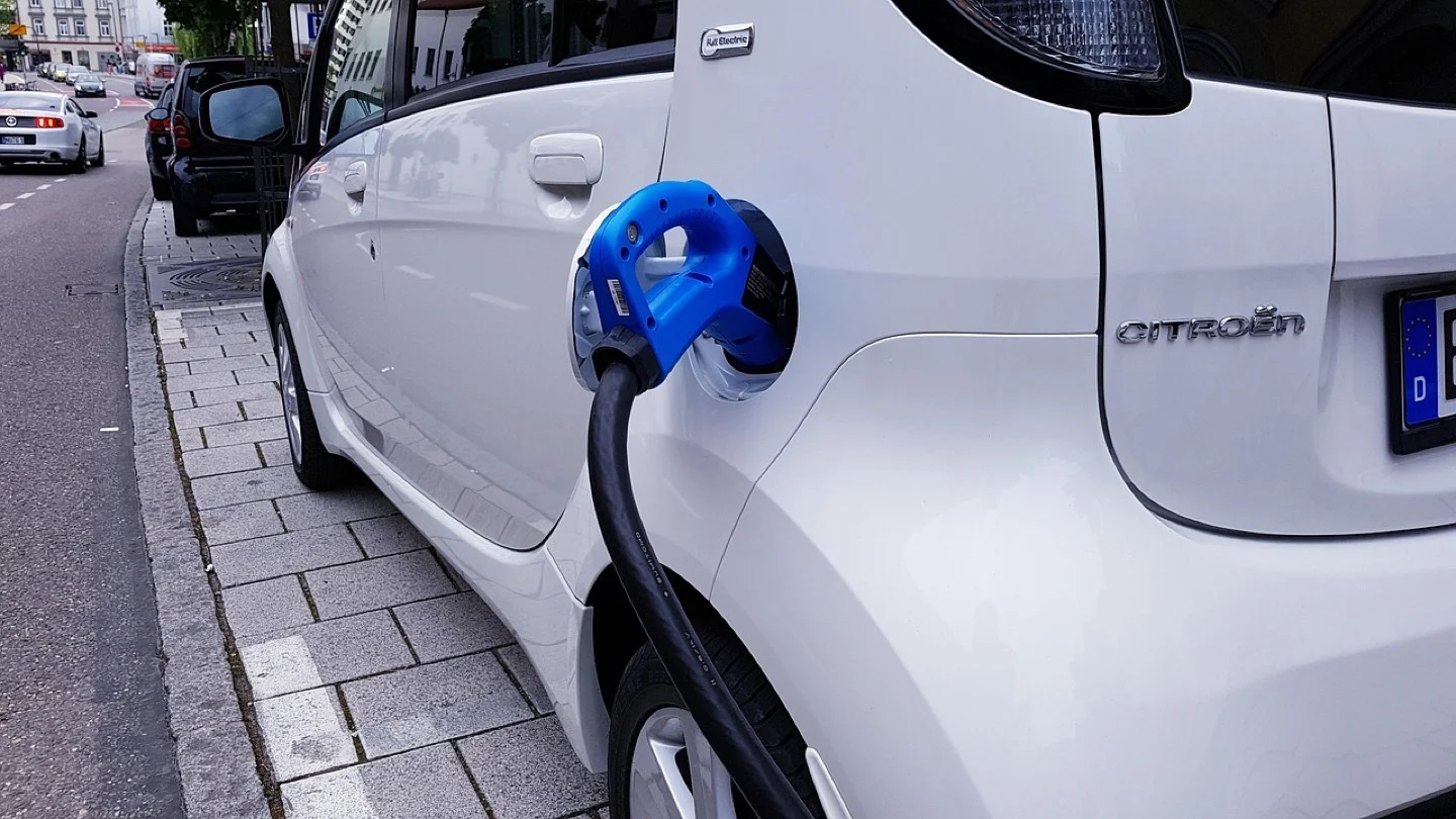 A white electric car is connected to a blue charging cable at the kerb.