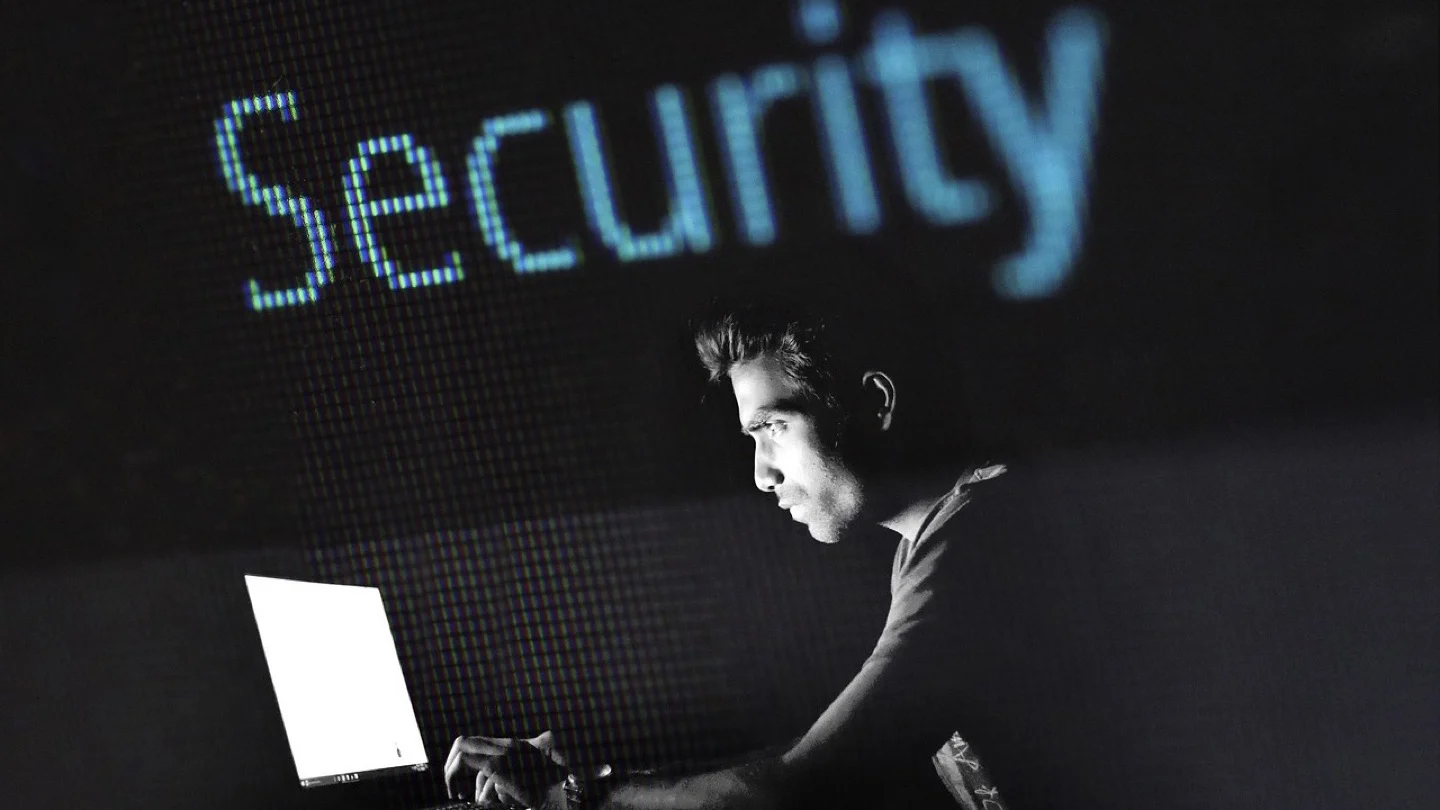 A cybersecurity professional works at a laptop against a dark digital security display.