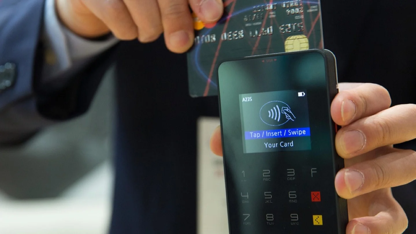 A payment card is held above a contactless payment terminal.