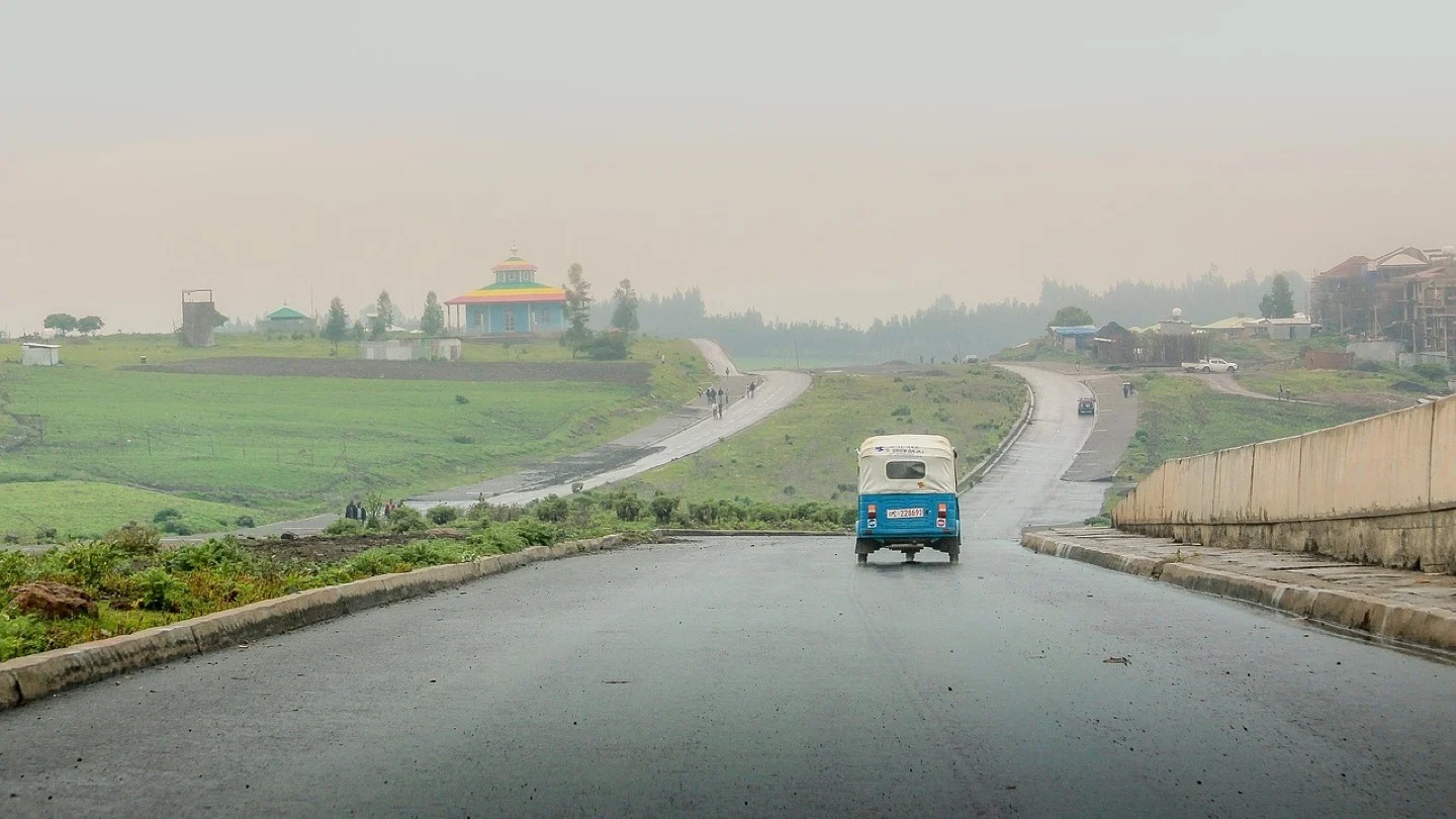 A blue three-wheeled vehicle travels along a wet road in Ethiopia.