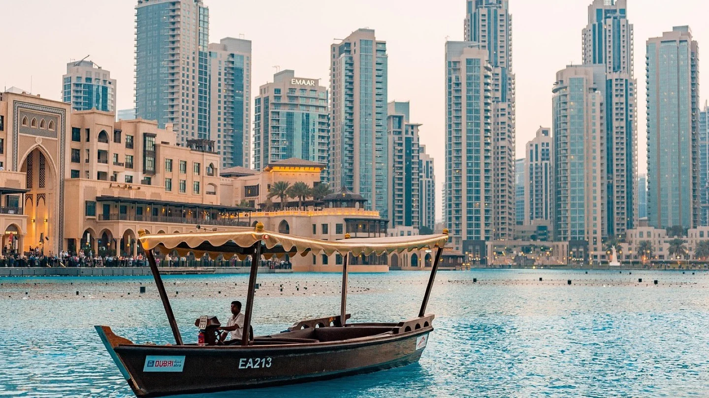 An abra crosses the water in downtown Dubai with high-rise buildings behind it.